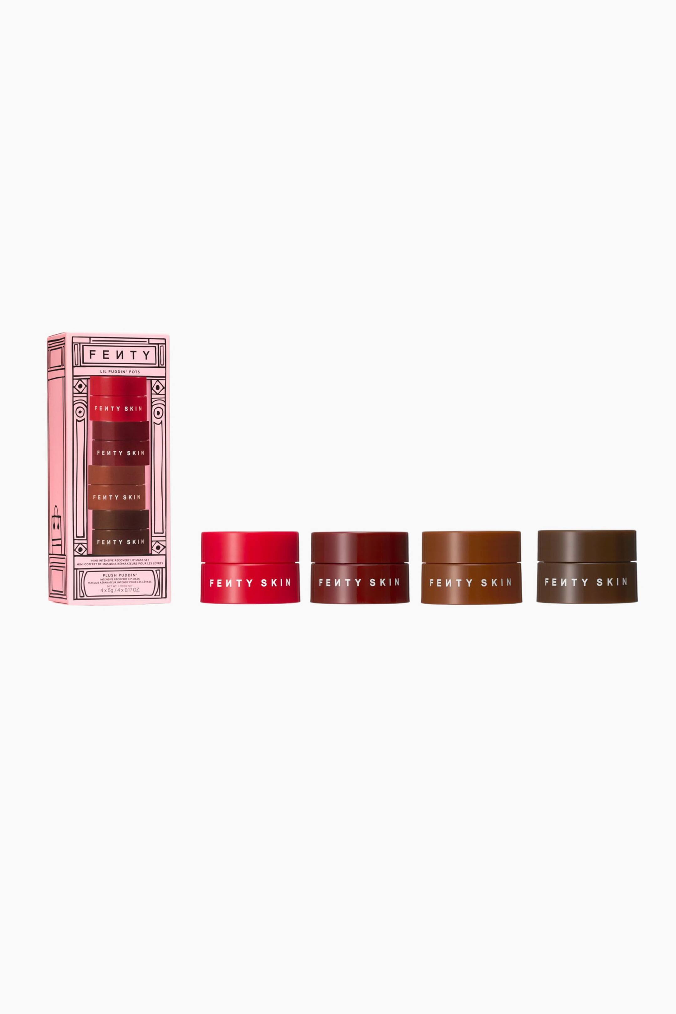 Visa större bild: Ett Fenty Skin läppmaskset visas med en ljusrosa rektangulär ask bredvid fyra små, cylindriska burkar placerade i en horisontell rad. Burkarna, var och en med logotypen "FENTY SKIN" i vit text, är färgade i klarrött, djup tranbärsröd, varm karamell och mörkbrun.