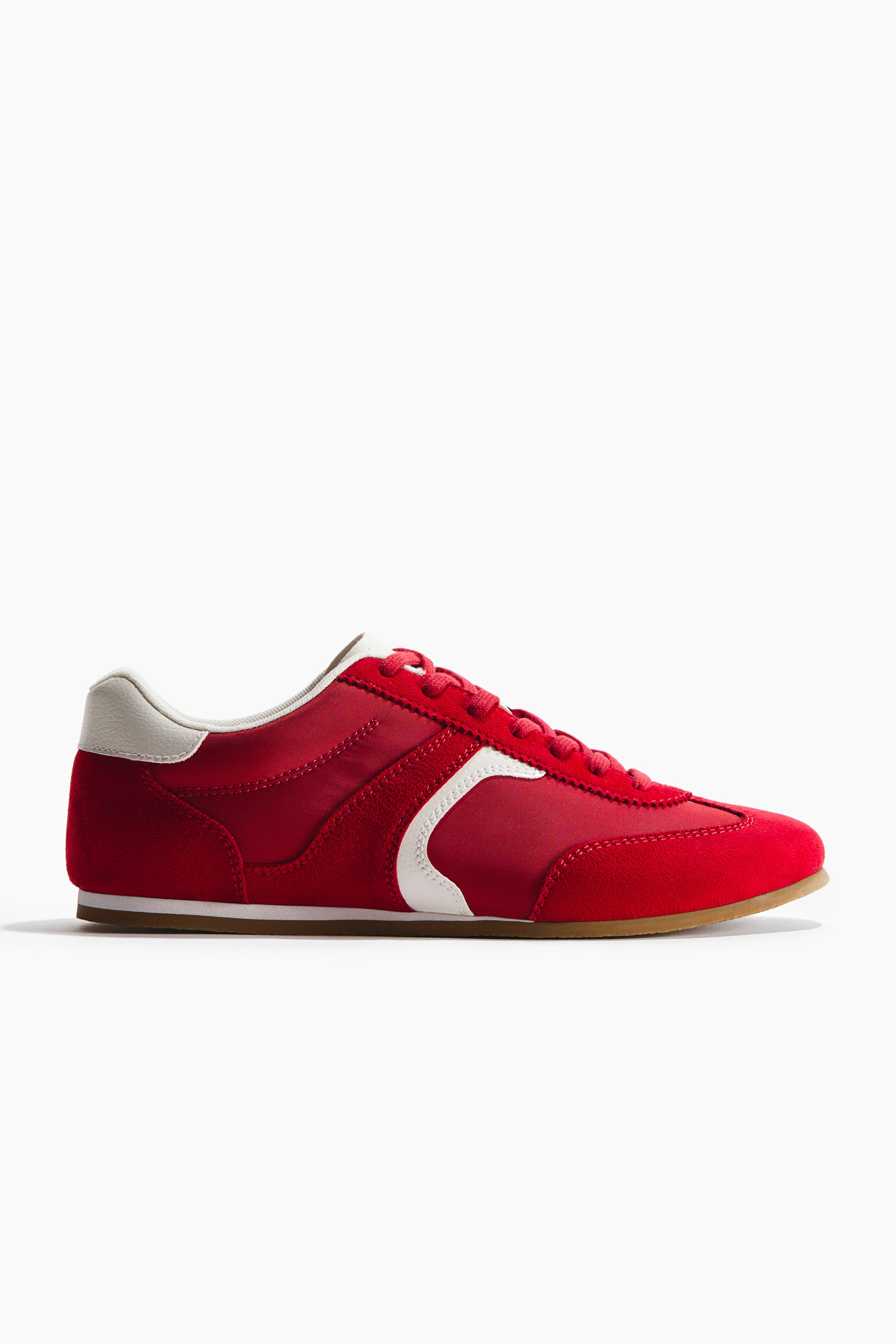 Grösseres Bild ansehen: Ein roter Turnschuh präsentiert sein Seitenprofil, mit einem gepolsterten oberen Rand, einer Zunge und roten Schnürsenkeln an der Vorderseite. Er zeigt rote Wildleder- und Textilpaneele, akzentuiert mit einem weißen geschwungenen Streifen an der Seite, einer weißen Fersenkappe und einer hellbraunen Laufsohle.