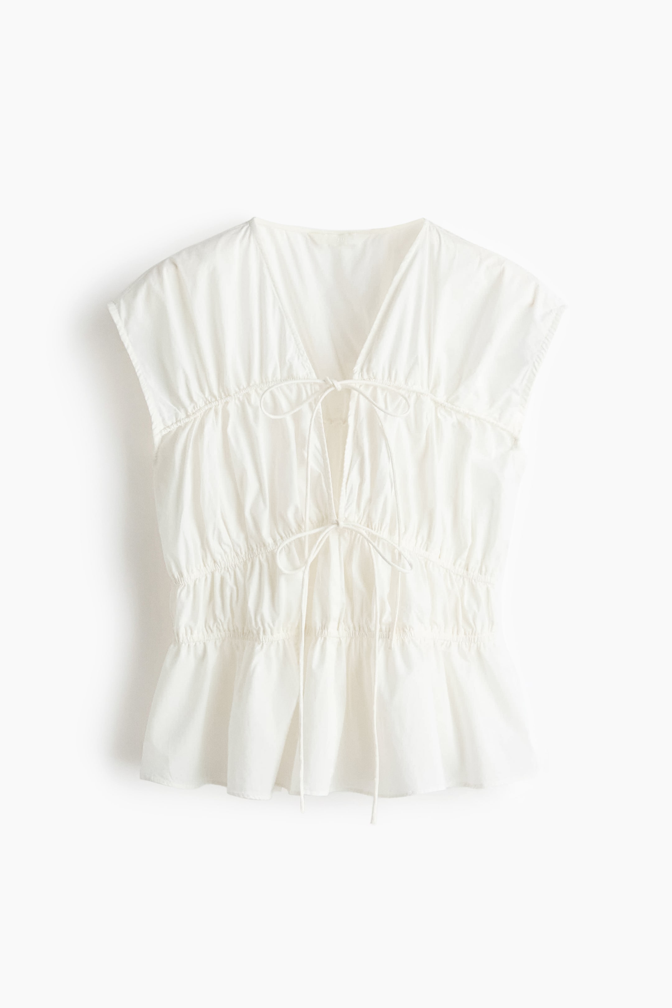 Xem ảnh lớn hơn: Một chiếc áo sơ mi trắng không tay đang trình bày mặt trước của nó, với một cổ chữ V sâu và hai hàng dây rút spaghetti buộc ở phía trước. Sự đàn hồi hẹp đang kết hợp với dây rút để tạo ra hiệu ứng nhún trên toàn bộ thiết kế, kết thúc với một phần peplum xòe nhẹ nhàng.