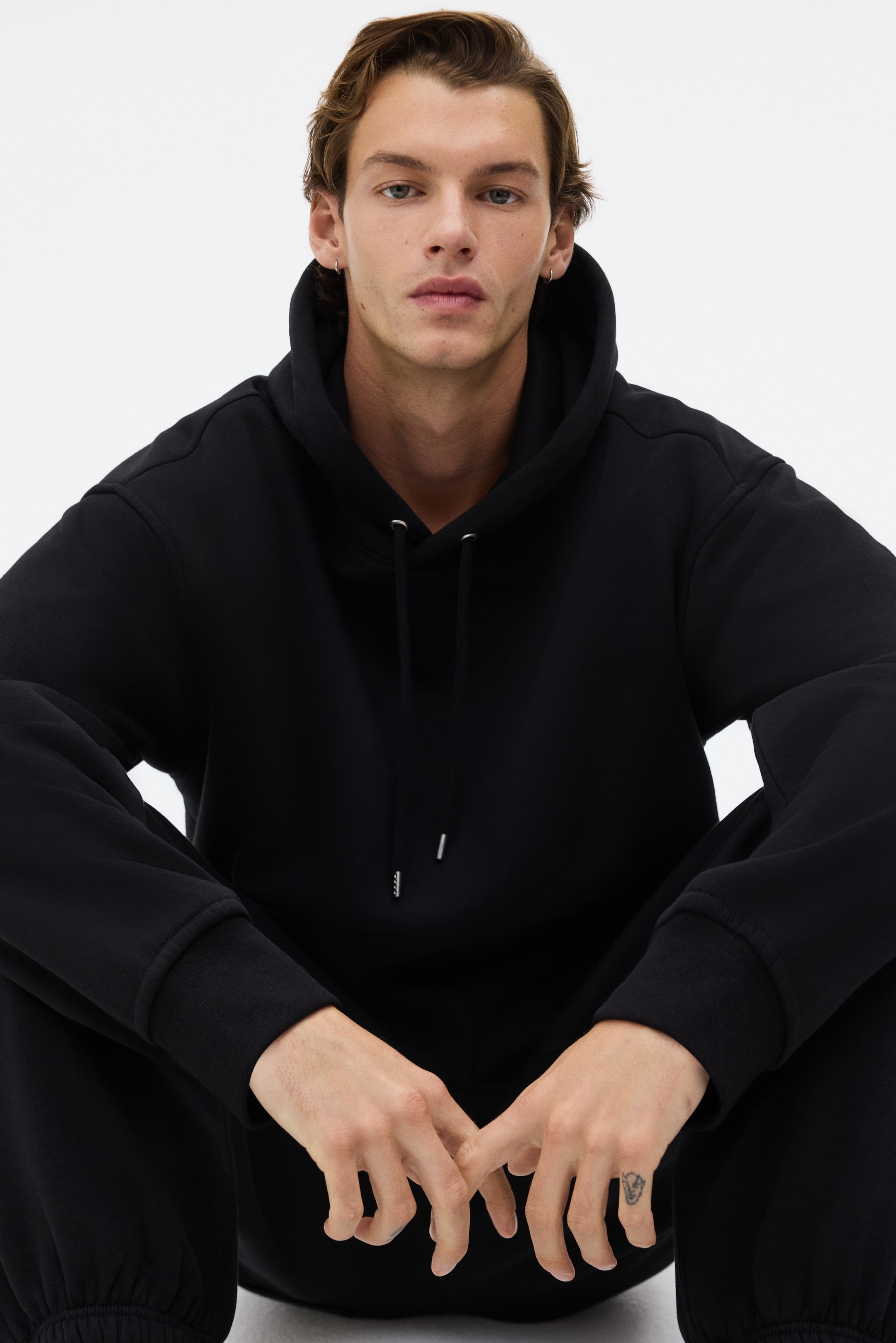 Visualizza immagine più grande: Una felpa con cappuccio nera viene presentata da un'angolazione frontale, con cappuccio a coulisse e terminali argentati. Presenta una vestibilità comoda con polsini a coste.