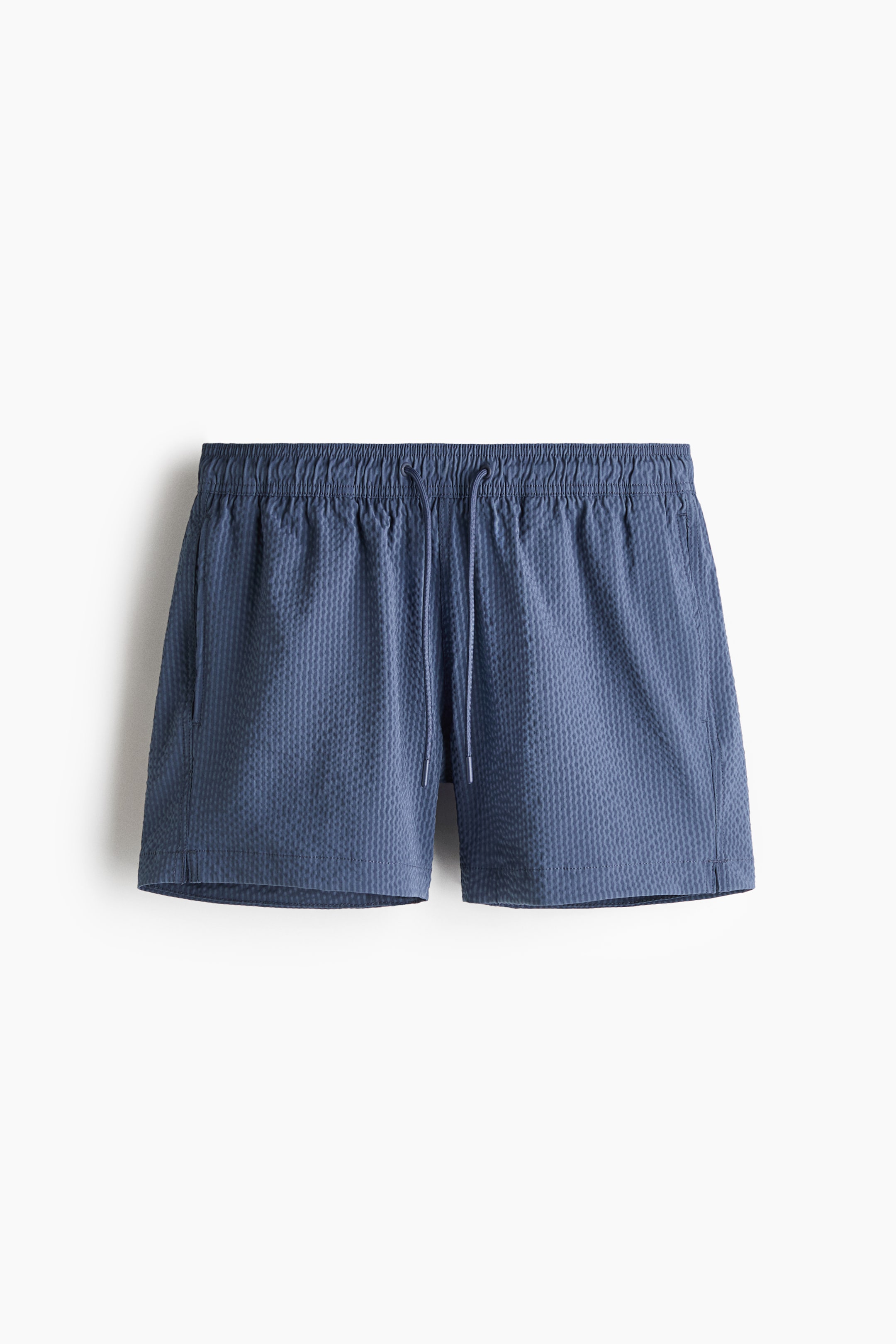 View larger image: Swim shorts are shown from the front, featuring a blue seersucker texture. They have a covered elastic waistband with a drawstring, side pockets, and small slits on each side of the hem.