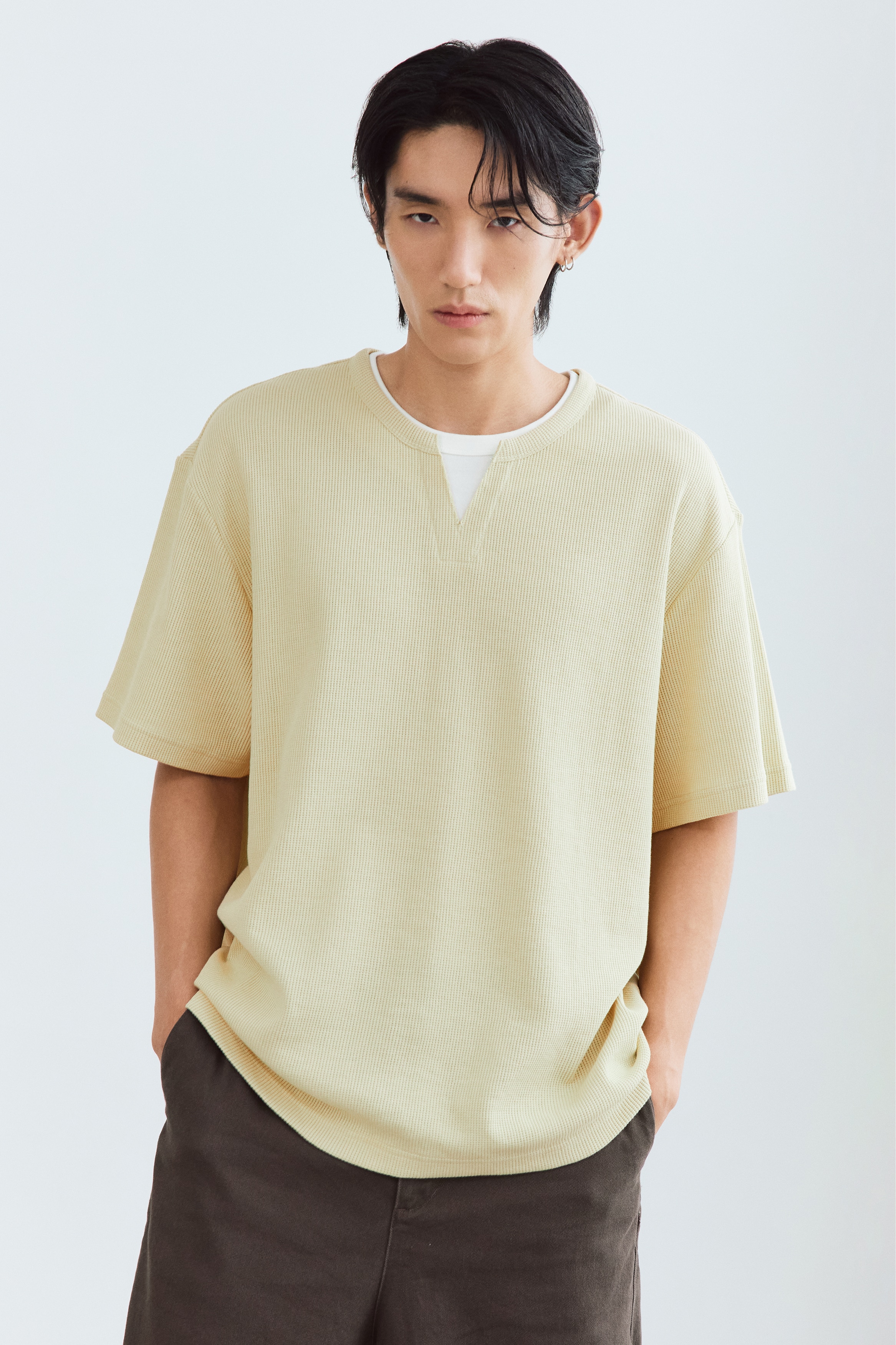 The light yellow, textured waffle-knit t-shirt is shown from the front, featuring a relaxed fit with loose short sleeves and a straight hem. A split-neck collar reveals a layered white crew neck collar underneath, creating a double-layered design.