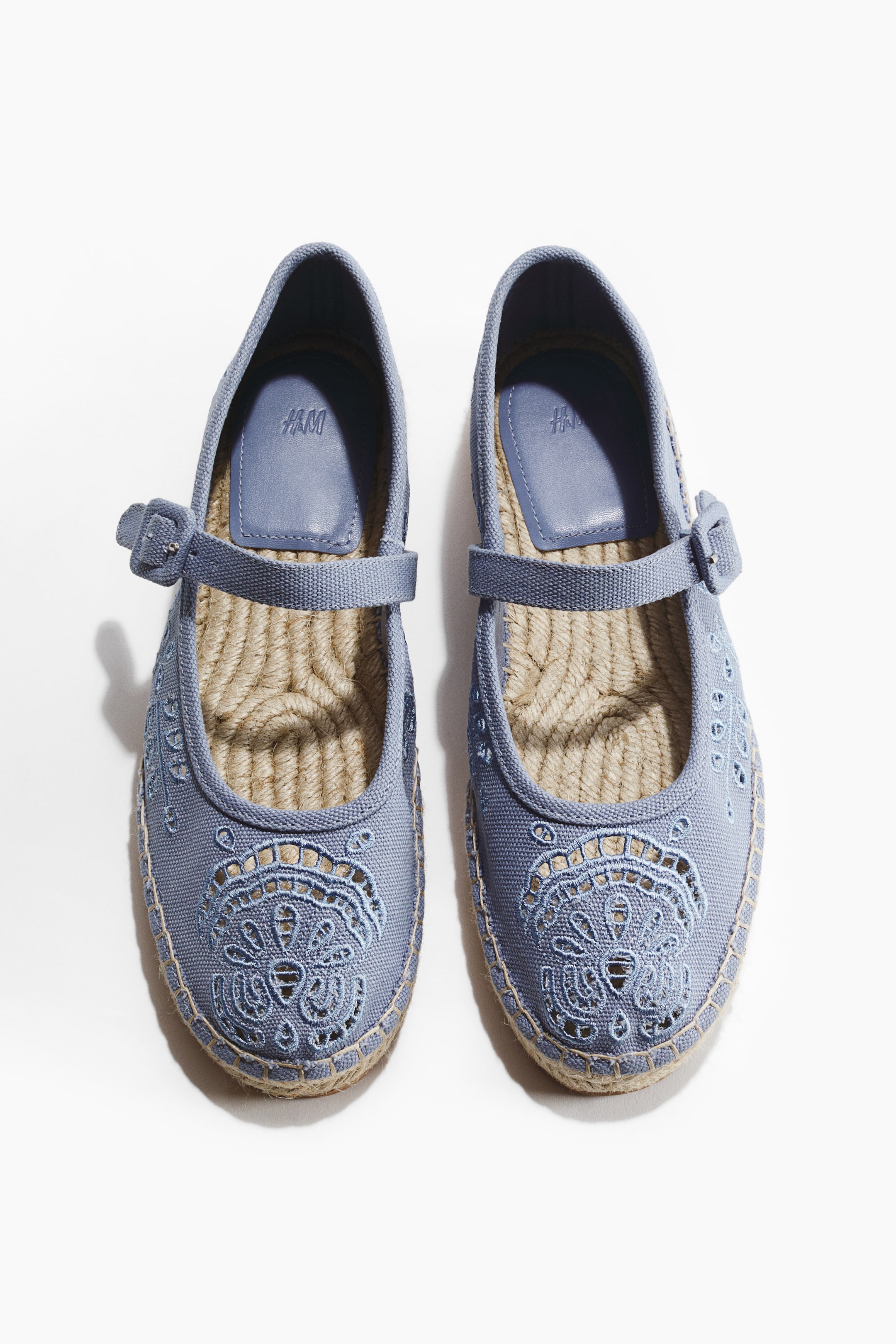 Zobrazit větší obrázek: Světle modré espadrilky s kulatou špičkou, nastavitelným páskem s přezkou přes nárt a proplétaným jutovým lemováním podrážky. Složitý vyšívaný vzor s výřezy zdobí oblast špičky.