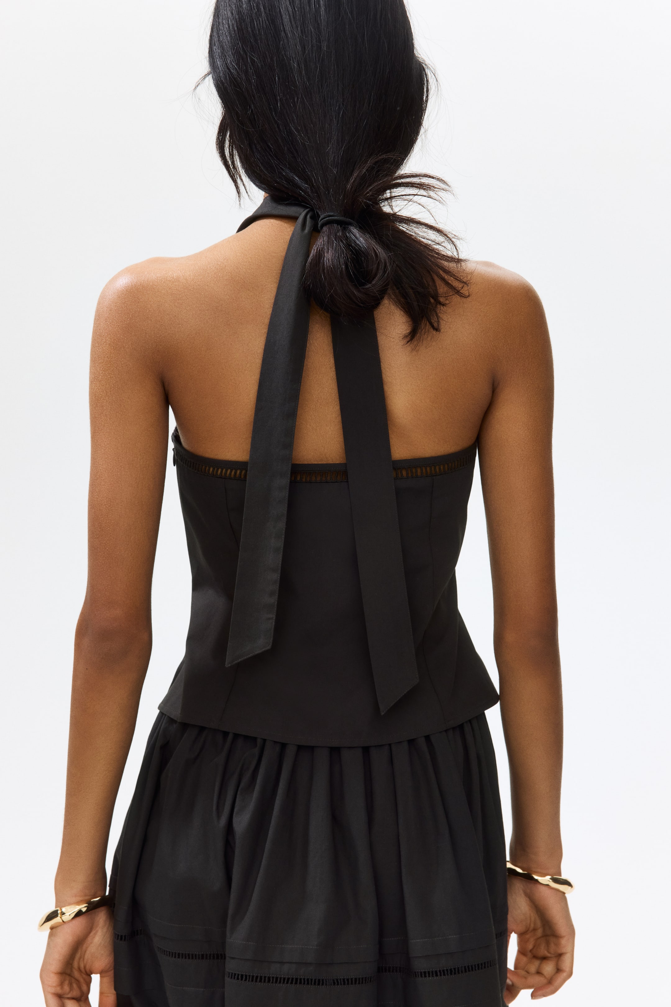 View larger image: "A black halter top features straps that tie at the back of the neck and a horizontal eyelet band across the upper back. It pairs with a black gathered skirt, showcasing horizontal eyelet detailing near its hem, all viewed from the back."