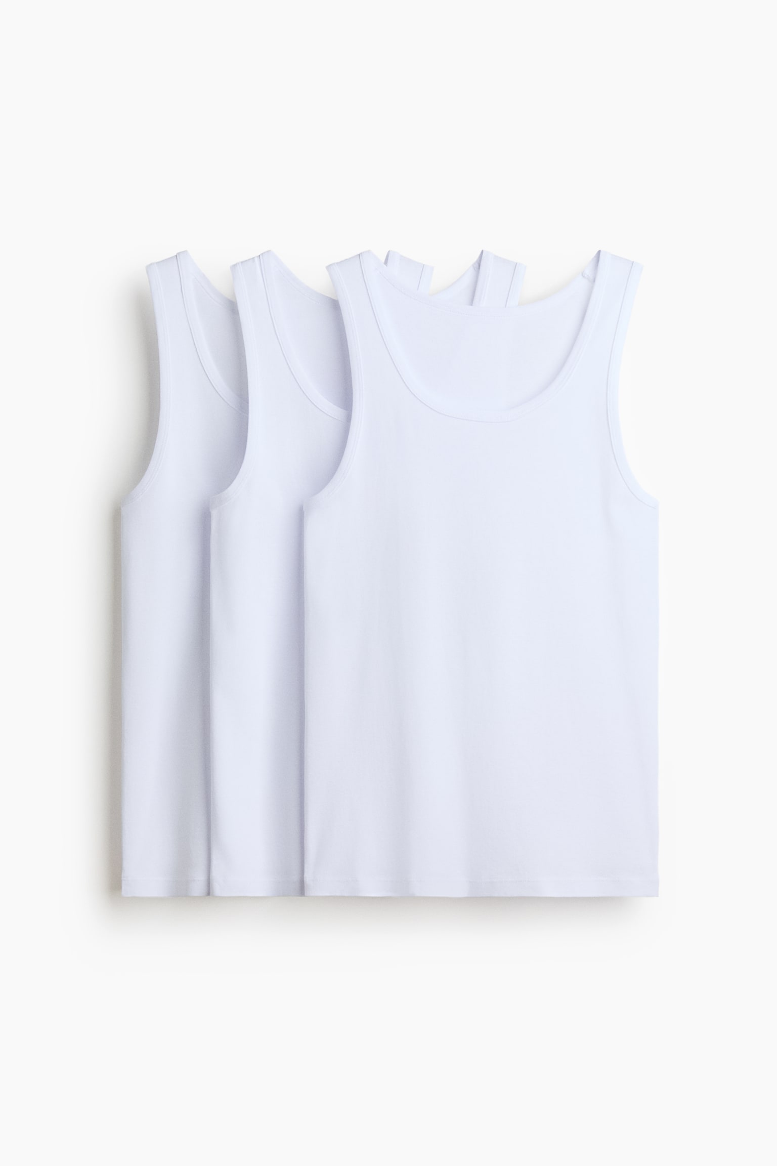 Three white singlets made from ribbed cotton jersey are displayed overlapping in a row, facing front. Each singlet features a deep round neckline, wide shoulder straps, and a straight hem.