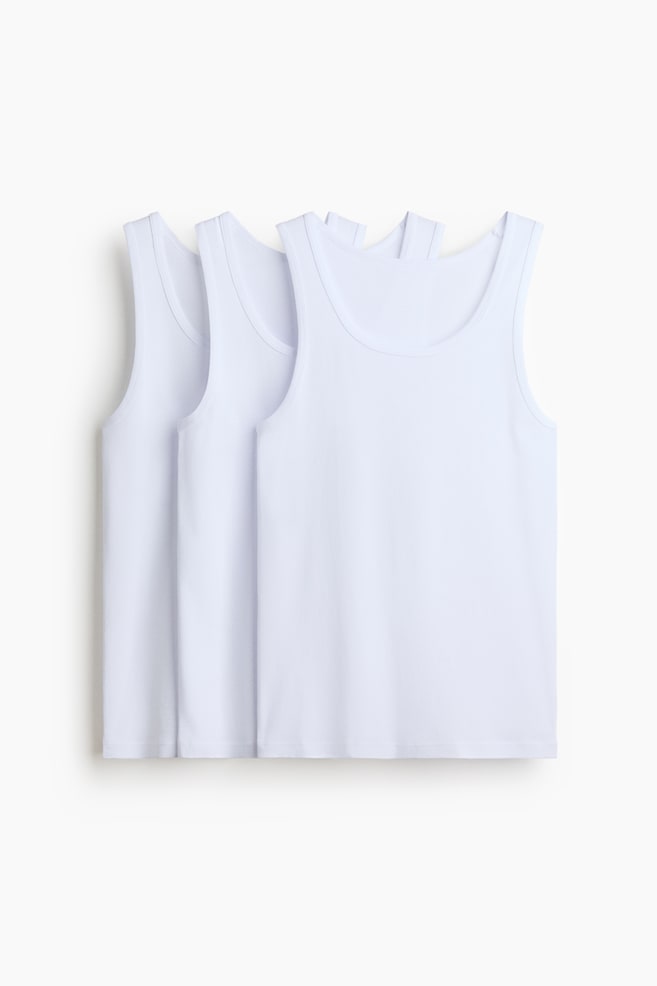 Tre hvite singletter i ribbestrikket bomullsjersey er vist overlappende pÃ¥ rad, vendt forover. Hver singlet har dyp rund hals, brede skulderstropper og rett nederkant. - 1