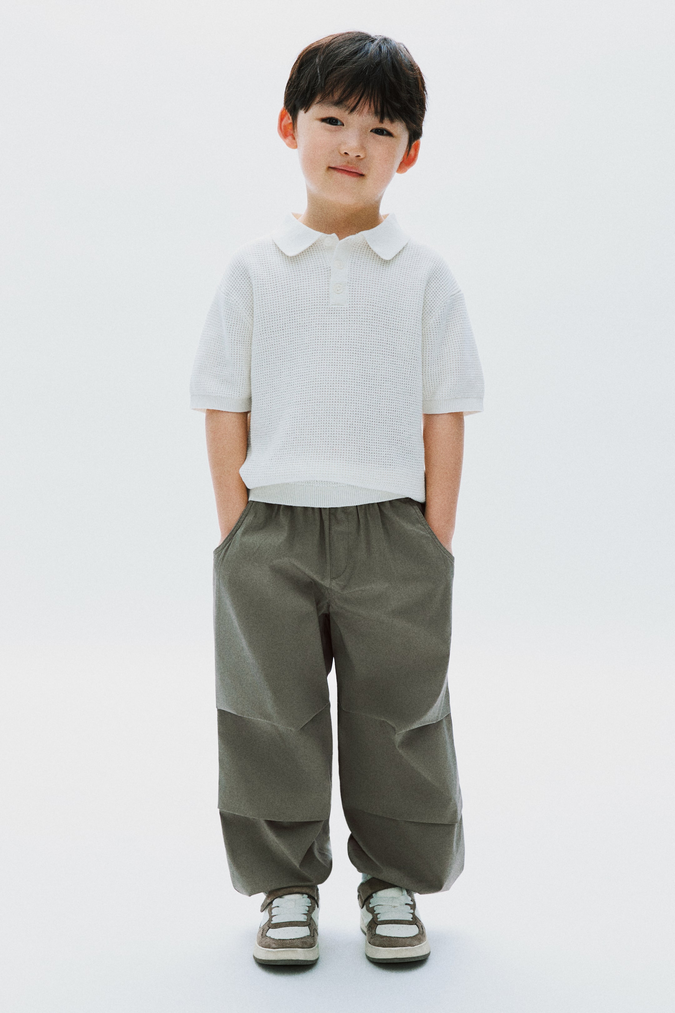 View larger image: A white perforated knit polo shirt with a two-button placket and short sleeves is being displayed, paired with olive green wide-leg pants featuring an elasticated waistband, side pockets, and paneling on the lower legs.