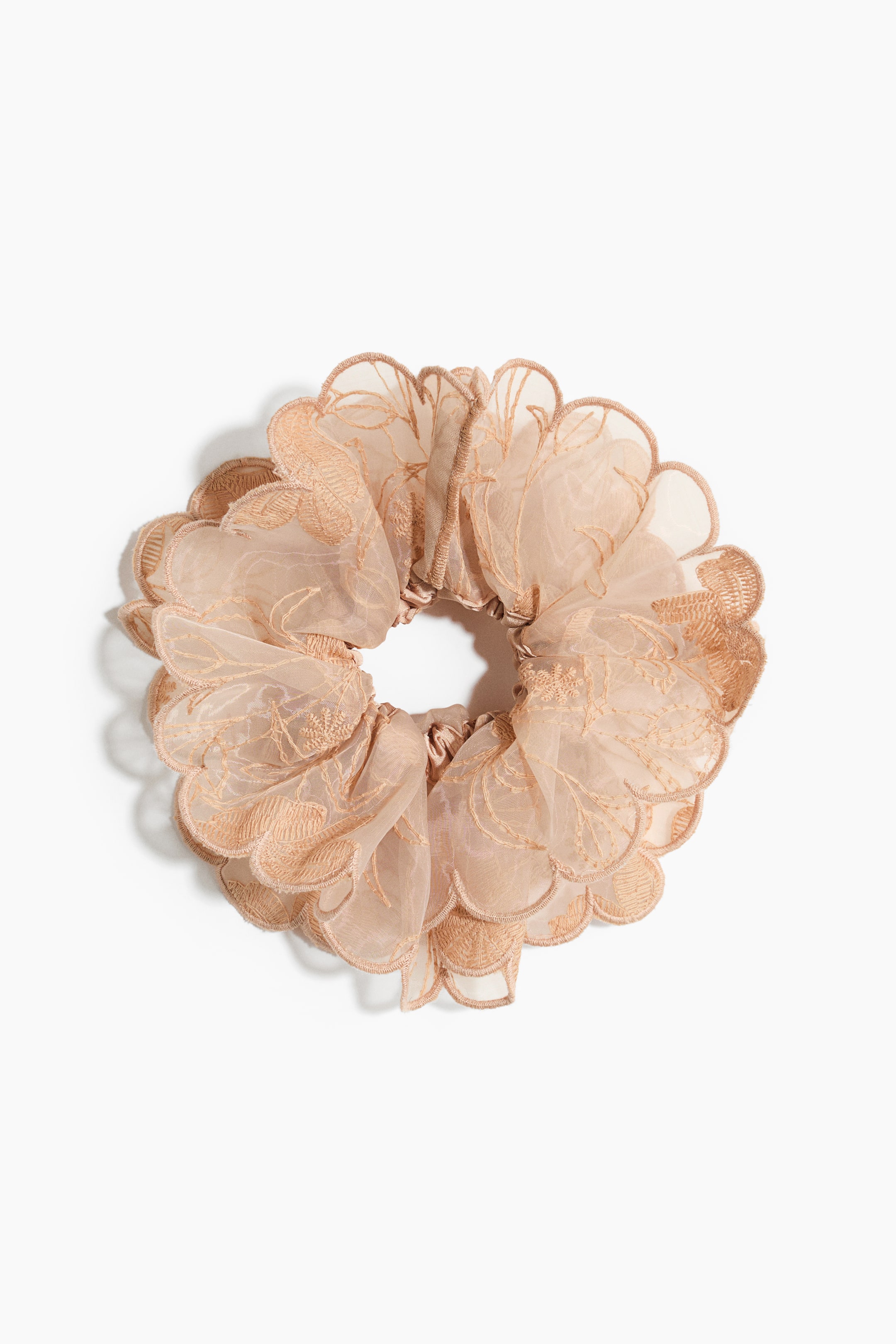 View larger image: A light beige scrunchie is displayed with a layered, sheer weave and embroidered pattern. It features overlocked, scalloped edges, forming a voluminous, ruffled shape.