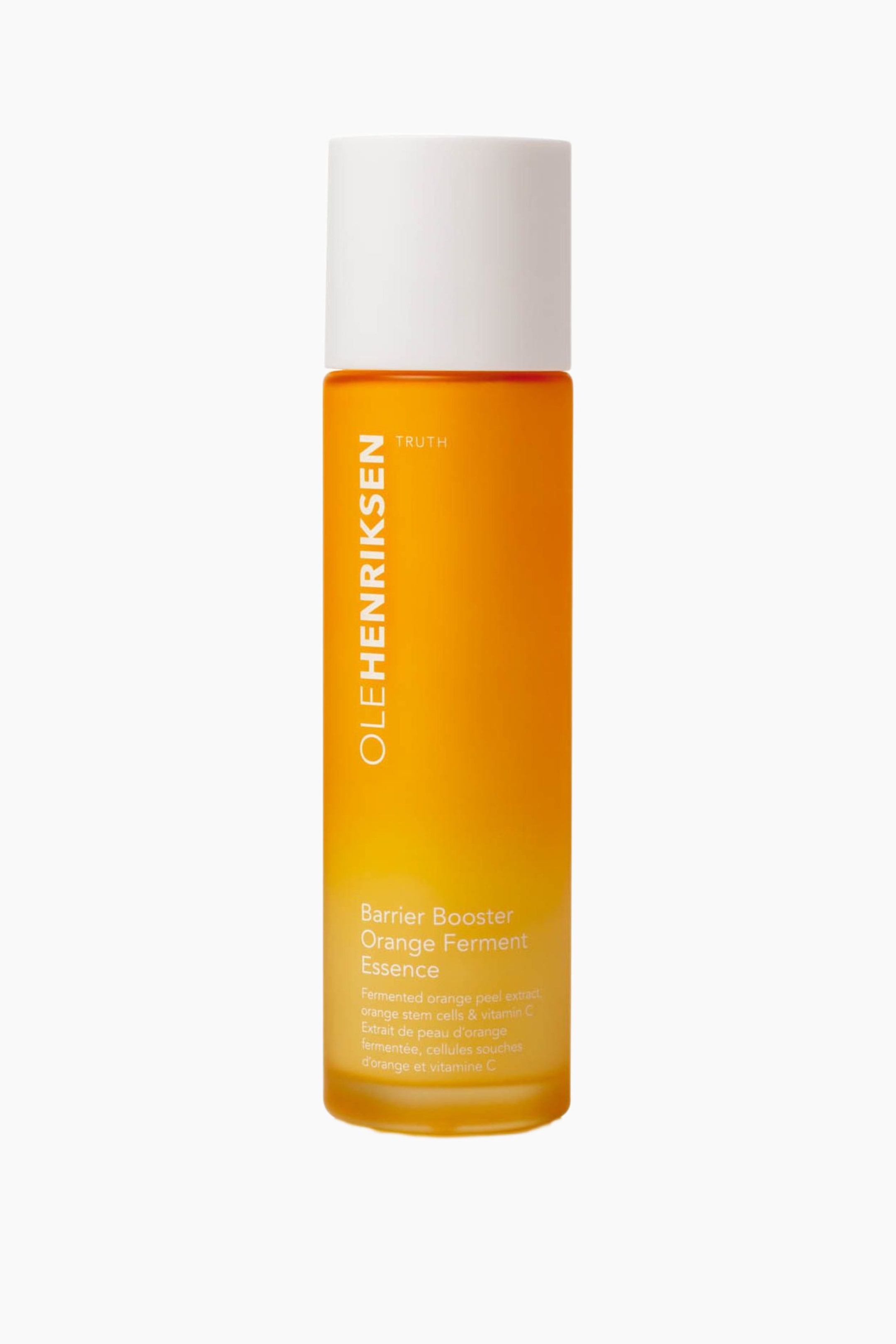 Vis større bilde: En Olehenriksen Barrier Booster Orange Ferment Essence-flaske står oppreist og viser sin sylindriske form med en oransje-gul gradientkropp og hvitt lokk. Hvit tekst på flasken viser «OLEHENRIKSEN» vertikalt, «TRUTH» horisontalt, samt «Barrier Booster Orange Ferment Essence» og detaljert ingrediensinformasjon.