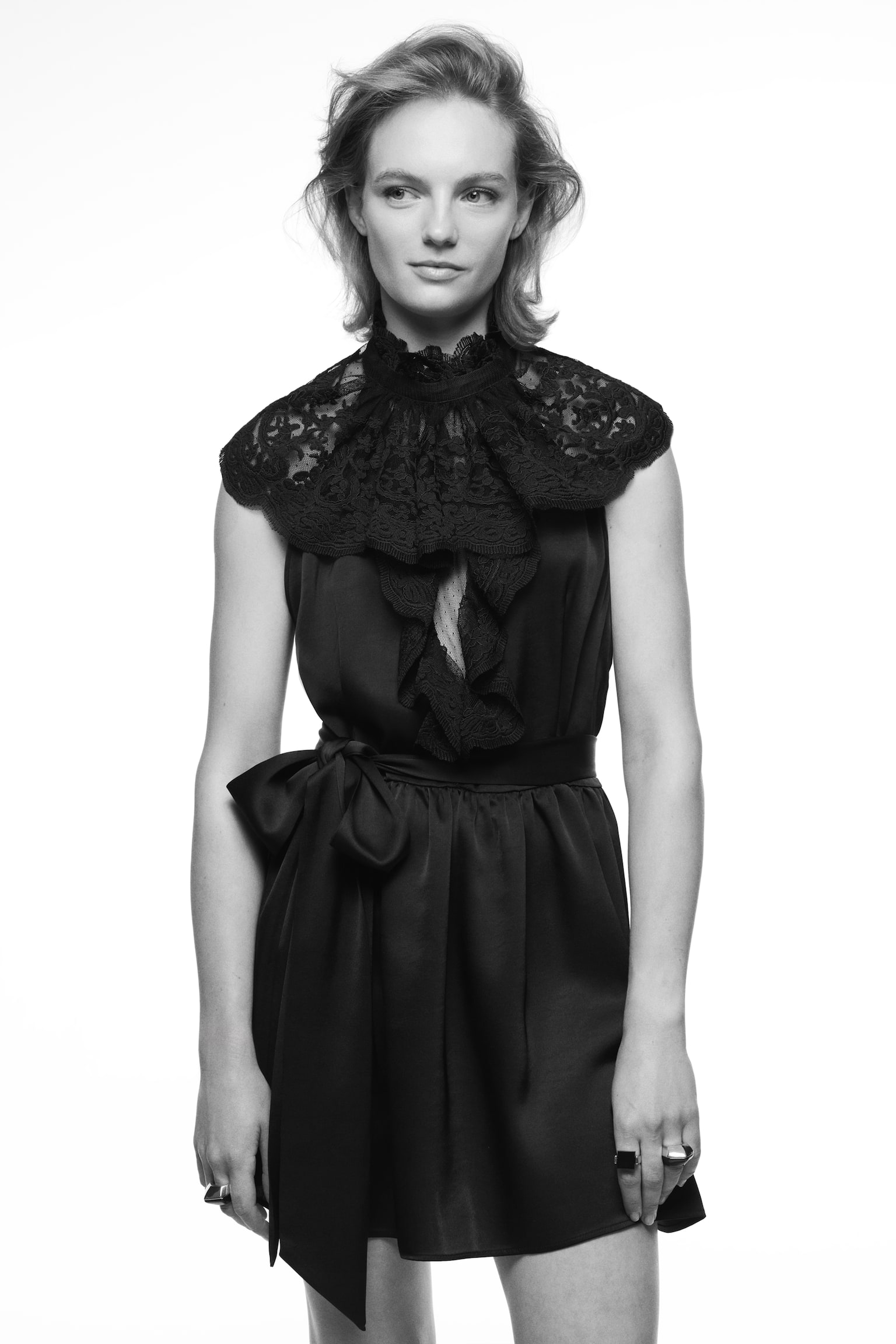 A black dress featuring a high, ruffled lace collar and an intricate lace design extending over the shoulders. The waist is cinched by a prominent satin bow, and the skirt flows into a flared silhouette. - 1
