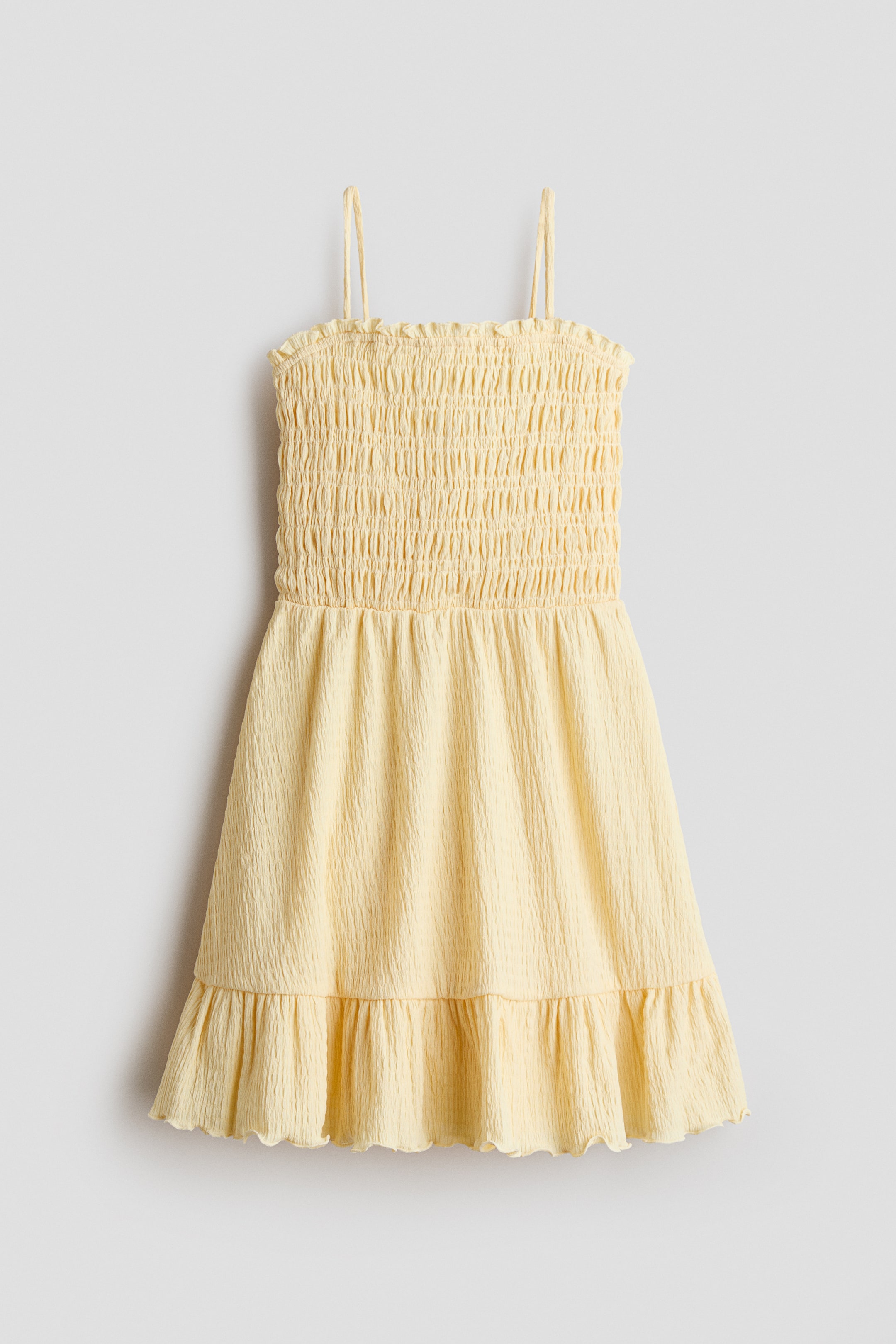 Grösseres Bild ansehen: Ein hellgelbes Minikleid zeigt seine Vorderseite, mit einem gesmokten Oberteil und dünnen Spaghettiträgern. Der Rock präsentiert eine geknitterte Textur und einen gerüschten Saum.