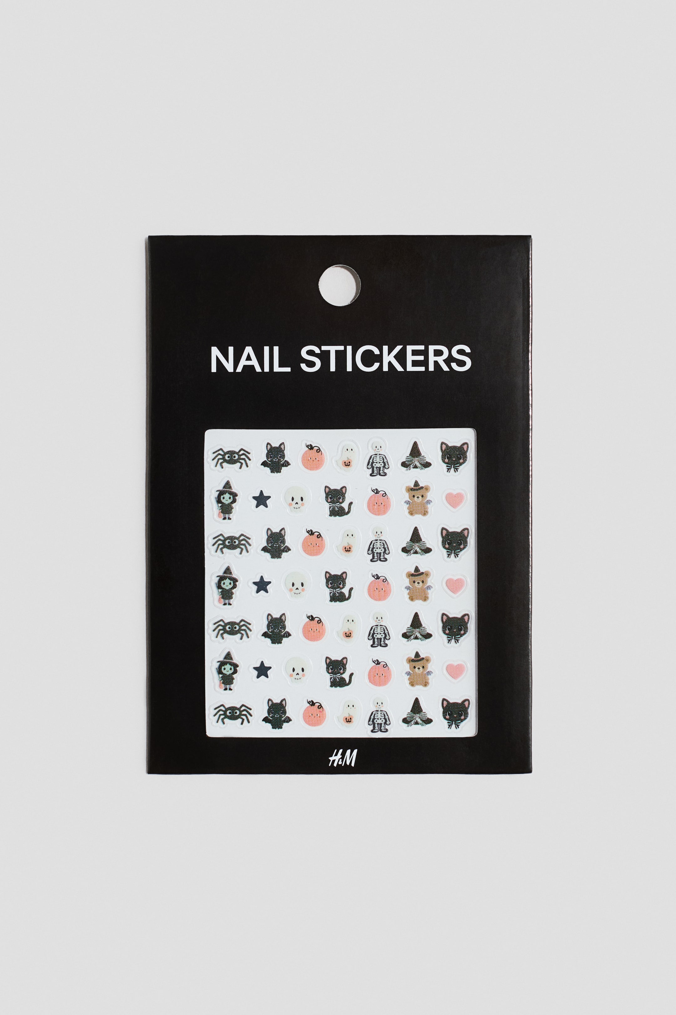 View larger image: Nail stickers are presented in a black rectangular packet, facing forwards, with a circular hang hole at the top. The packet displays "NAIL STICKERS" in white text above a clear window revealing rows of small Halloween-themed stickers, including spiders, black cats, pumpkins, skeletons, witches' hats, teddy bears, stars, and hearts.