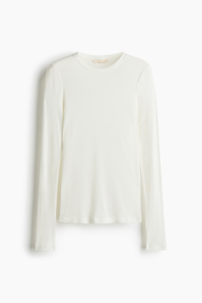 En tætsiddende, off-white, ribbet langærmet top vises fra FRONTEN. Den har en rund, ribkantet halsudskæring og ekstra lange ærmer. - 1