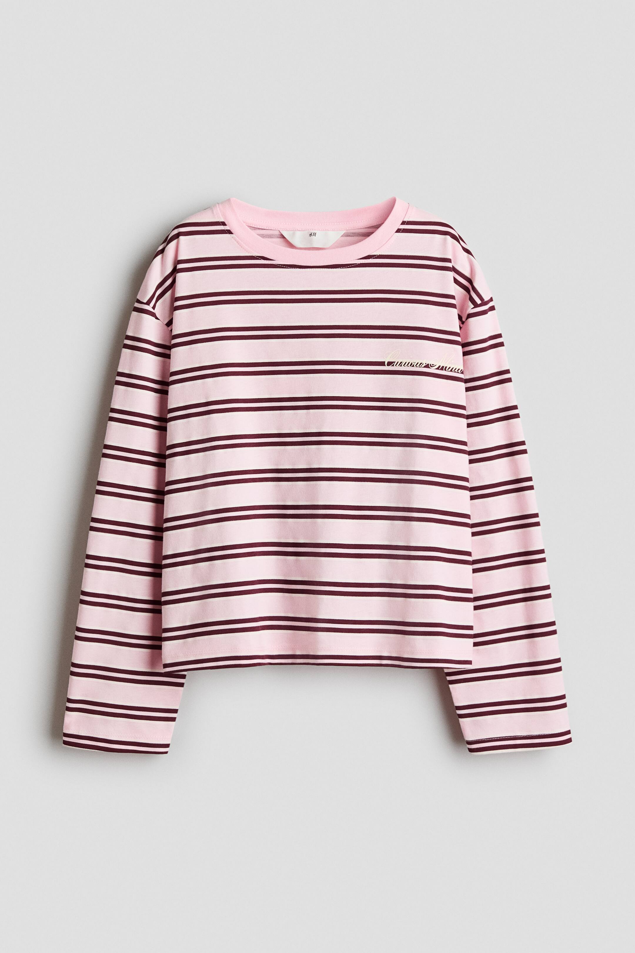 View larger image: A light pink long-sleeved T-shirt featuring horizontal maroon stripes is shown from the front. It has a relaxed fit with dropped shoulders, a ribbed crew neck, and small cursive script embroidered on the left chest.