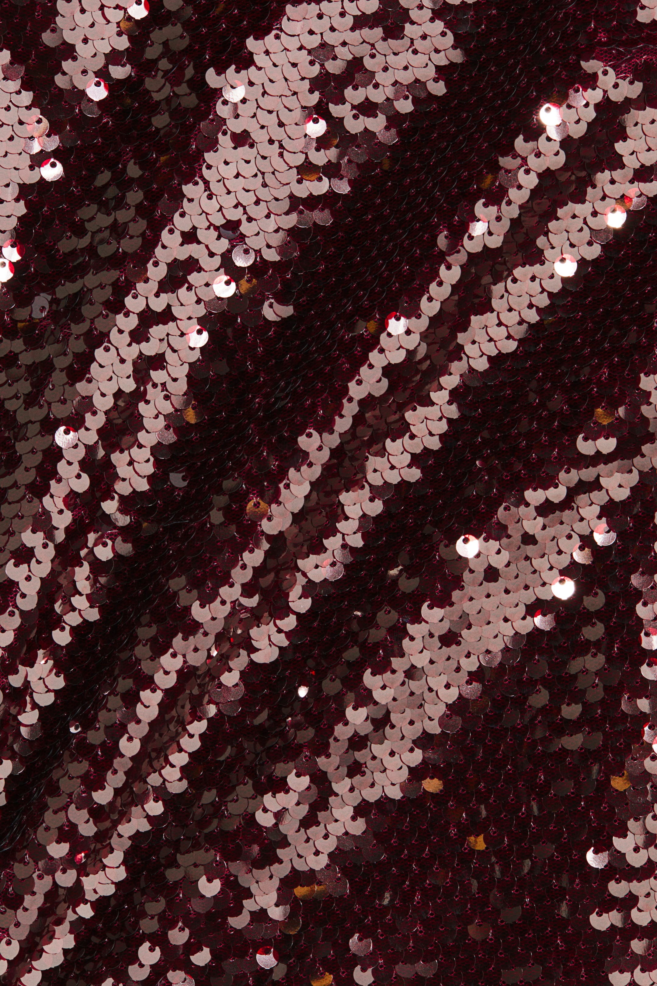 View larger image: Burgundy sequin fabric is showing shimmering round sequins that are overlapping, creating a textured surface with diagonal light patterns.