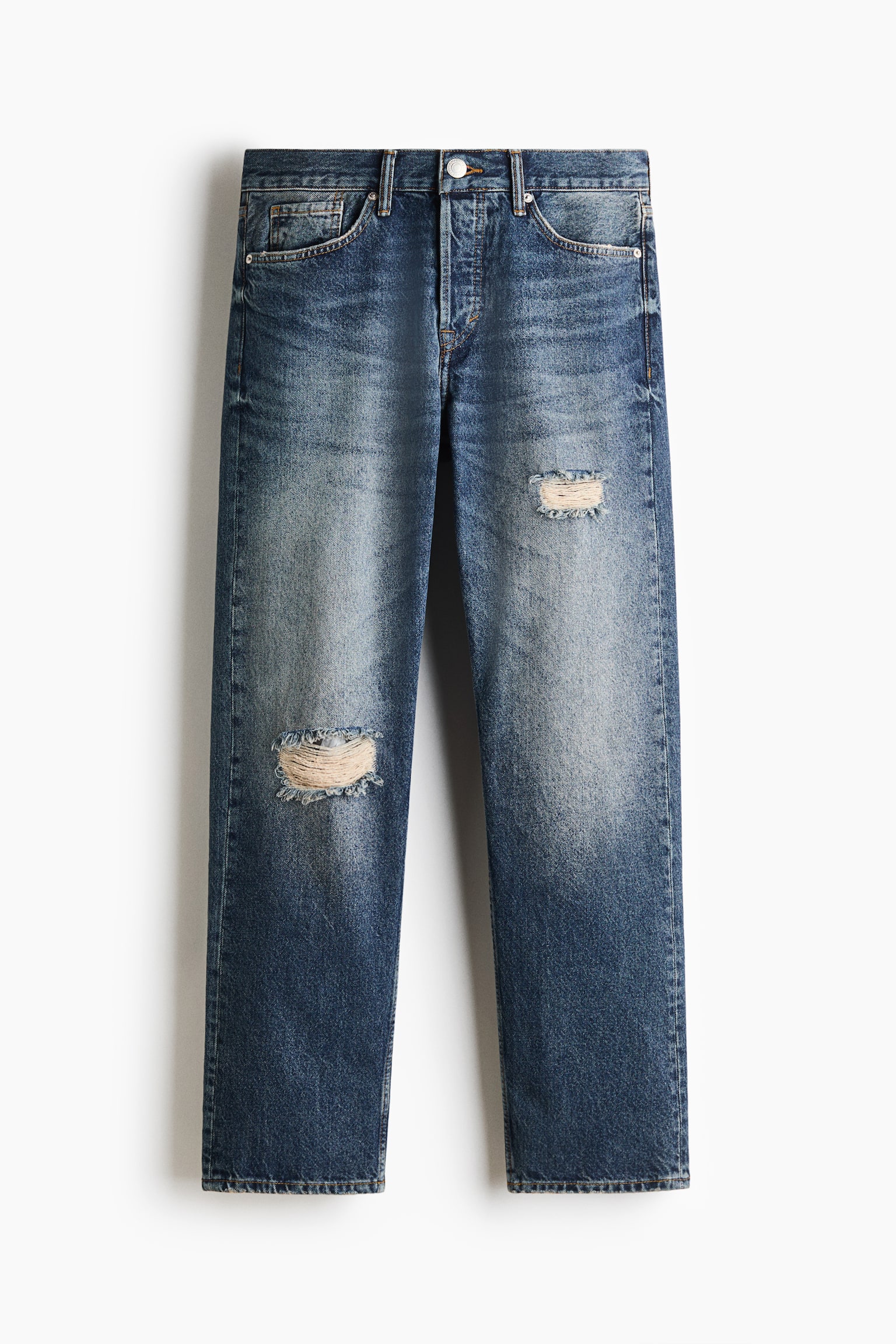 Et par straight-leg denimjeans hÃ¦nger fladt i frontvendt visning og viser en mellemblÃ¥ vask med falmede detaljer pÃ¥ lÃ¥rene. Jeansene fremviser en klassisk femlomme-stil, en knaplukning i ÑÐ°Ð»jen og to distressed-huller med synlige hvide trÃ¥de pÃ¥ forbenene.