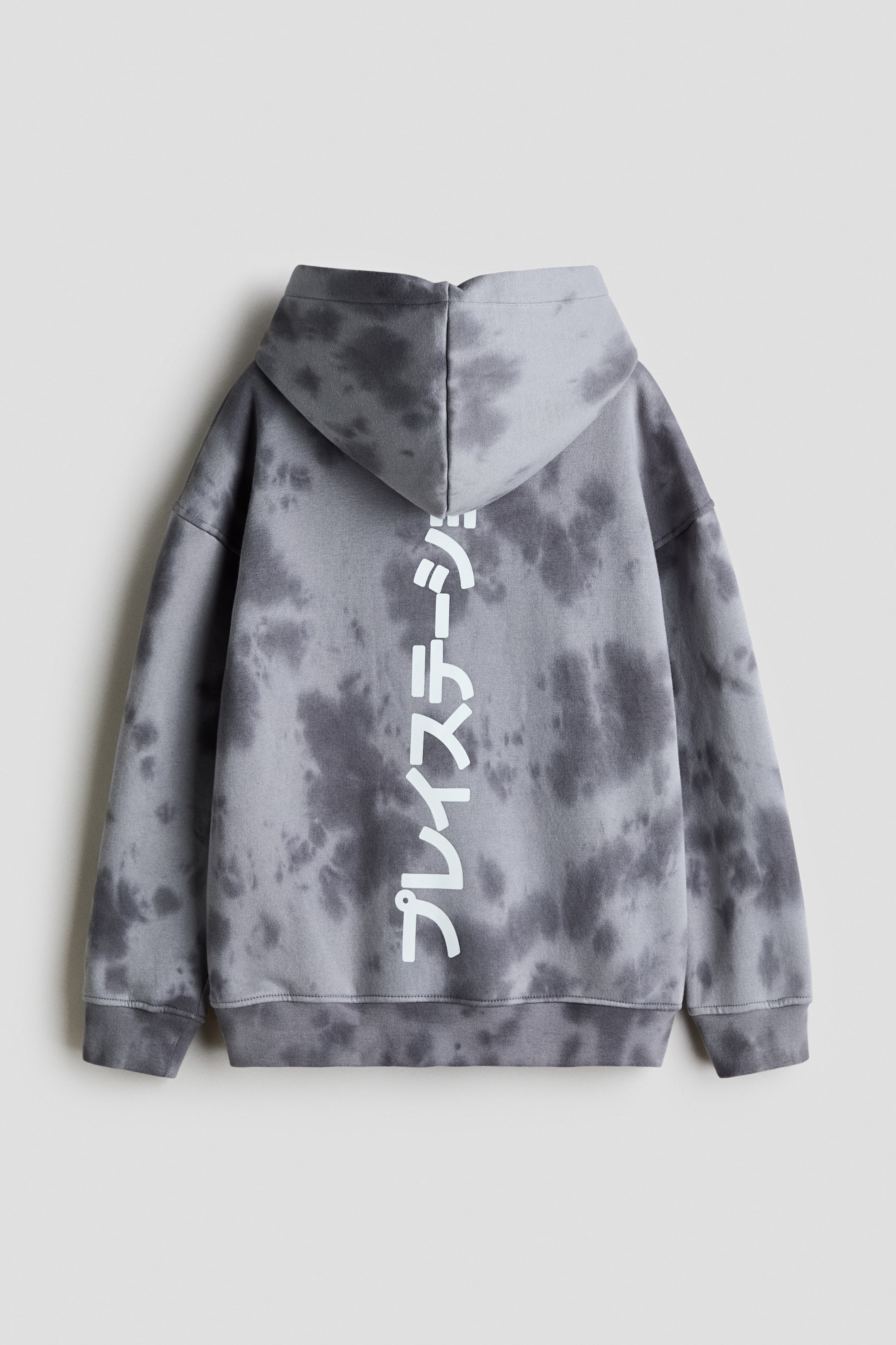 View larger image: A loose-fit hoodie with a grey and dark grey tie-dye pattern is shown from the back, featuring a lined hood, dropped shoulders, and ribbed cuffs and hem. A vertical print of white Japanese characters runs down the centre of the back.