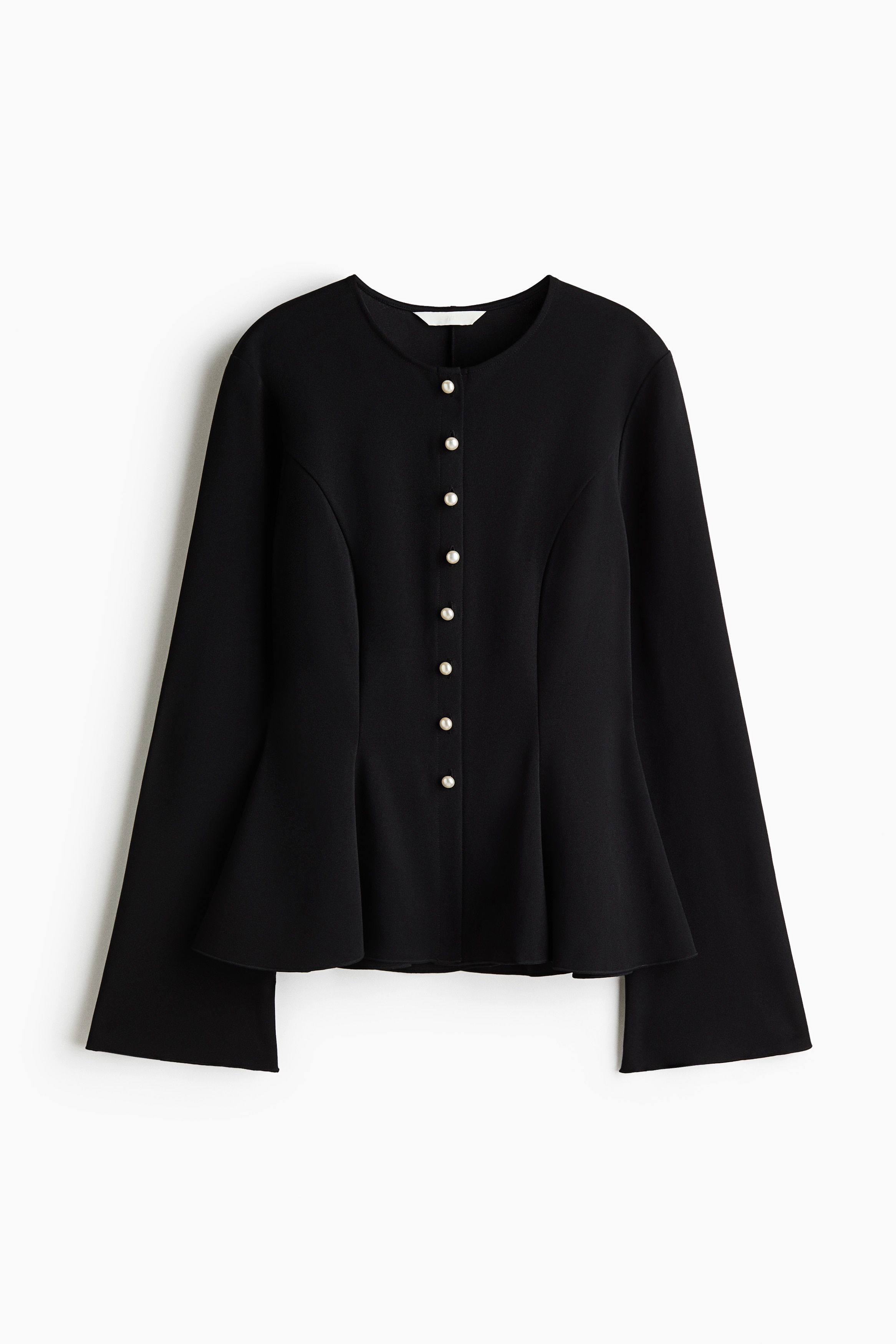 A black, long-sleeved peplum top is worn by the model, featuring a fitted silhouette, a collarless neckline with a small front slit, and a row of white pearl-like buttons. The top is paired with dark blue denim jeans.