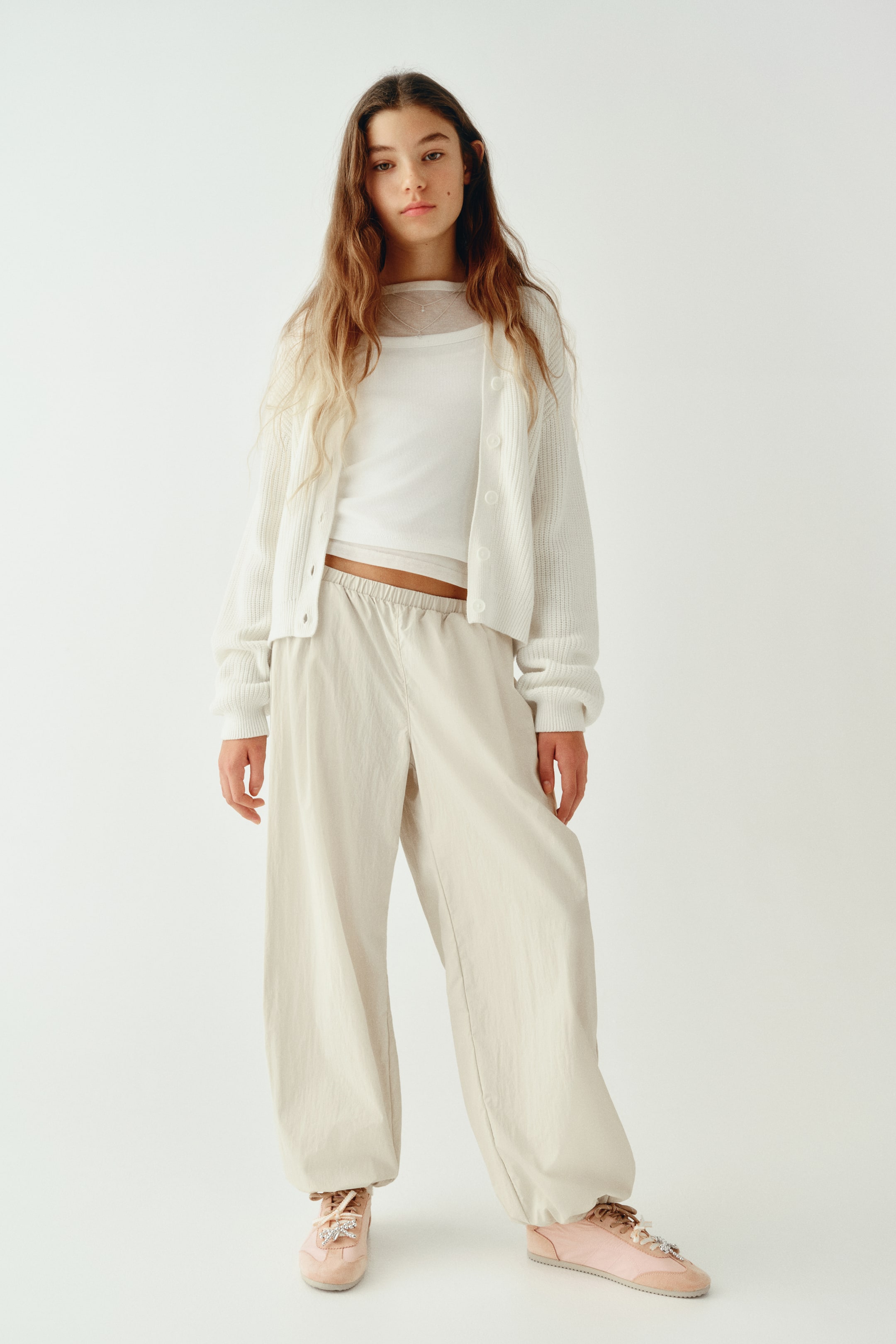 Visualizza l'immagine ingrandita: Pantaloni loose-fit in tessuto stropicciato beige chiaro, ripresi frontalmente, con vita elasticizzata e gamba ampia a palloncino che si restringe verso orli arricciati alle caviglie. I pantaloni cadono morbidamente, mettendo in risalto la silhouette rilassata e la texture leggera.
