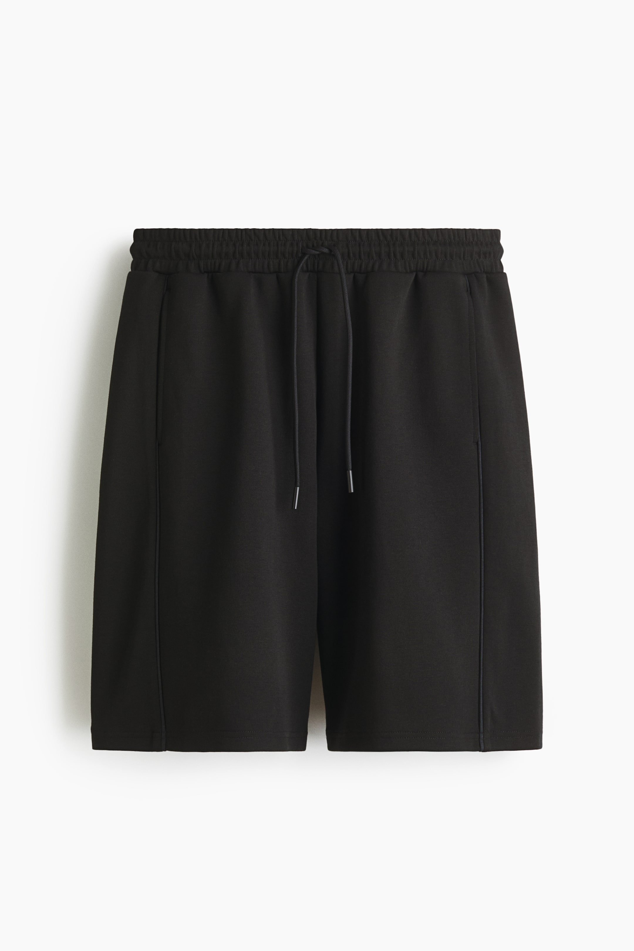 Zobacz większy obraz: Czarne szorty z elastycznym pasem i czarnym sznurkiem z srebrnymi końcówkami. Pionowe szwy biegną wzdłuż przodu każdej nogawki, a boczne kieszenie są widoczne.