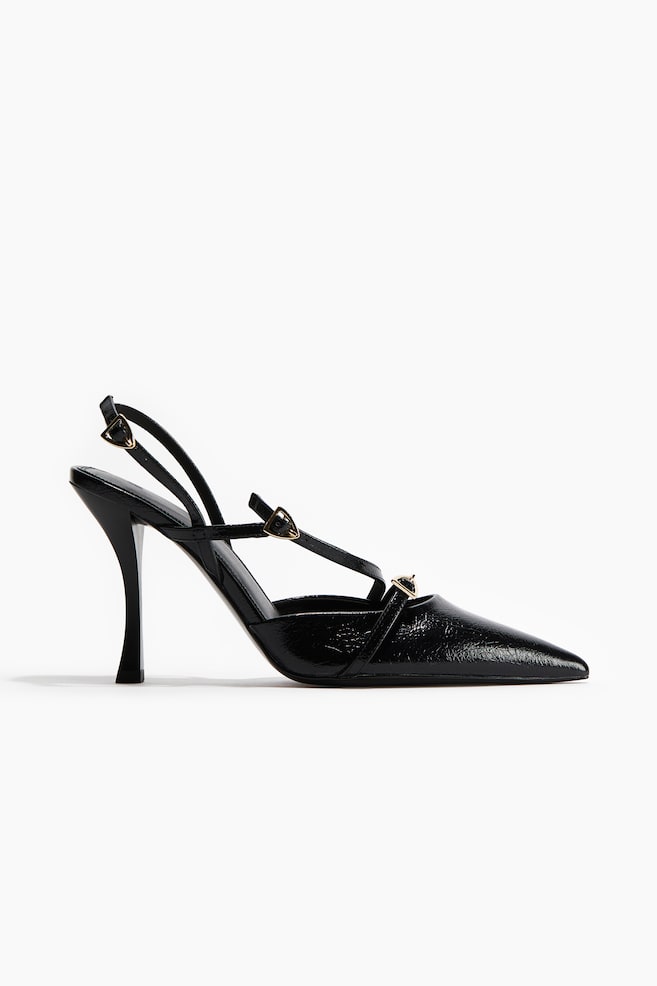 Ein schwarzer High-Heel-Pumps wird im Seitenprofil gezeigt, mit einer spitzen Zehenpartie und einem glänzenden, geknitterten Material. Dünne Riemen kreuzen sich über dem Rist und bilden einen Slingback, verziert mit kleinen goldfarbenen Schnallen. Der Schuh ruht auf einem hohen, skulpturalen ausgestellten Absatz. - 1