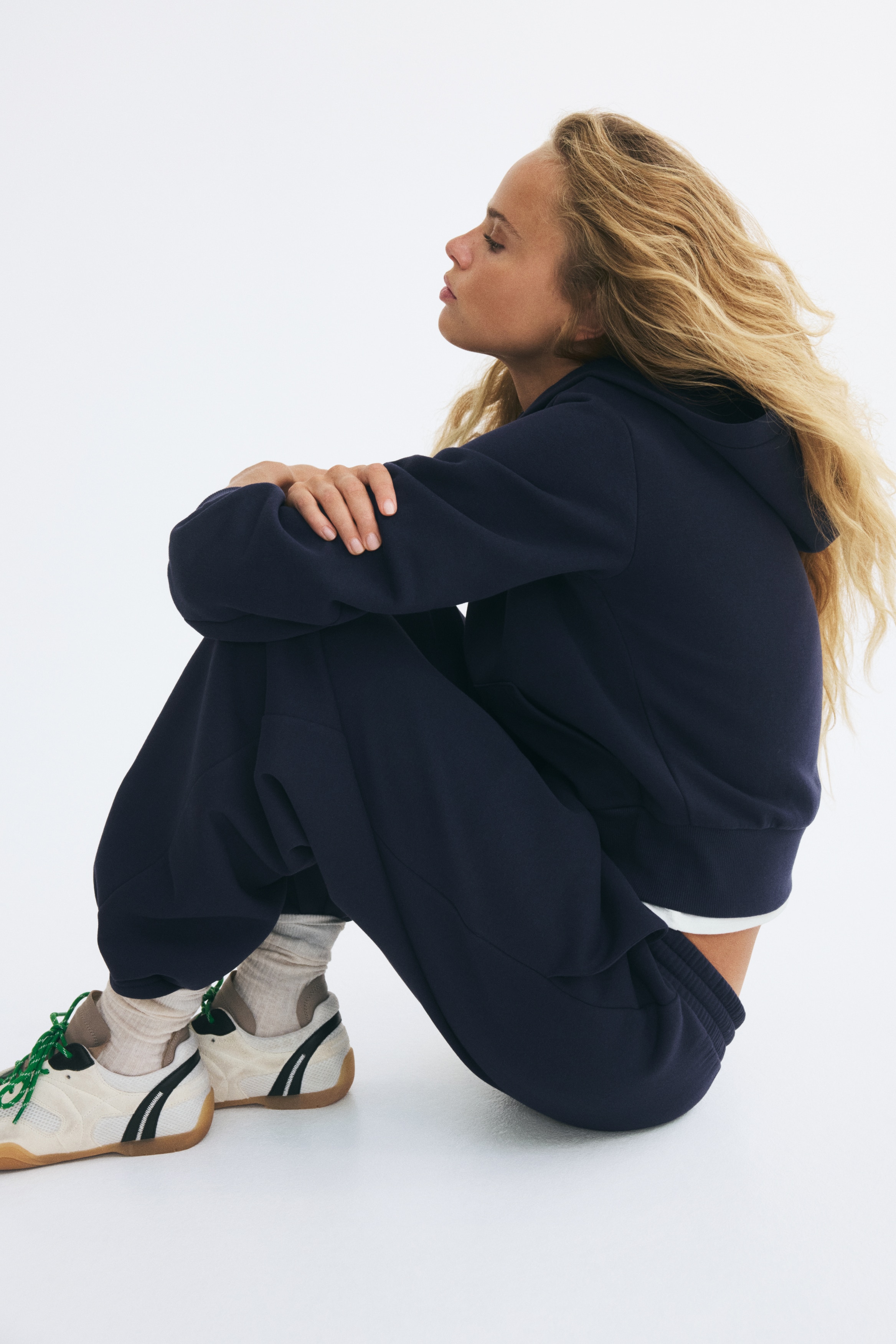Navy blue sweatpants are shown from the front, featuring a relaxed, structured fit with an elasticated ribbed waistband and matching drawstrings. The design shows side slip pockets and clean-finished, open hems at the ankles.