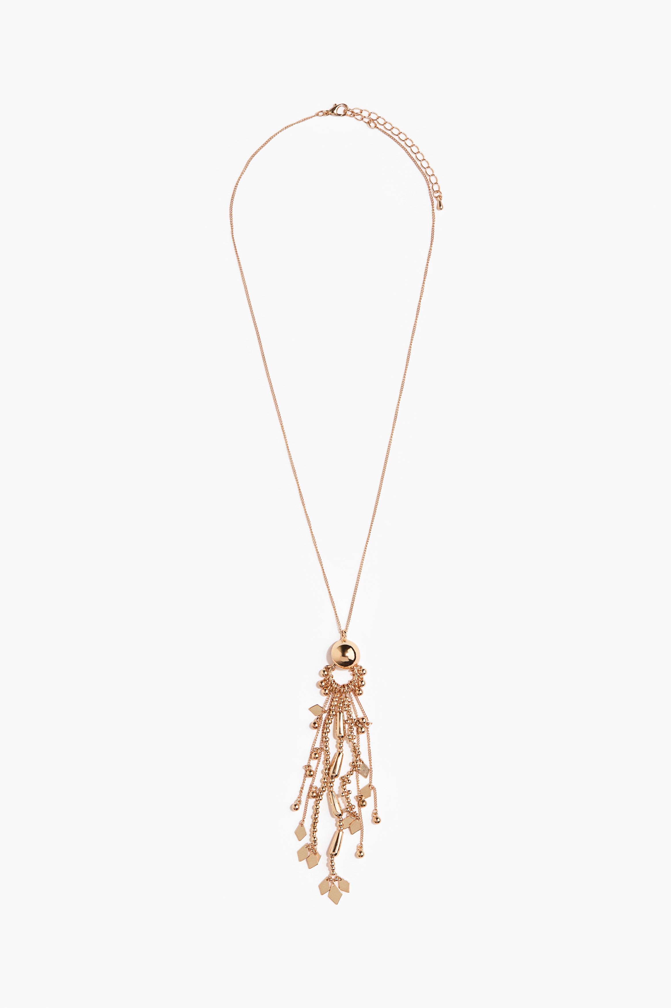 A long metal chain necklace featuring a gold-toned spherical bead and a multi-strand chain tassel is being worn by the model. The necklace hangs over a black cropped top layered under a matching open cropped jacket.