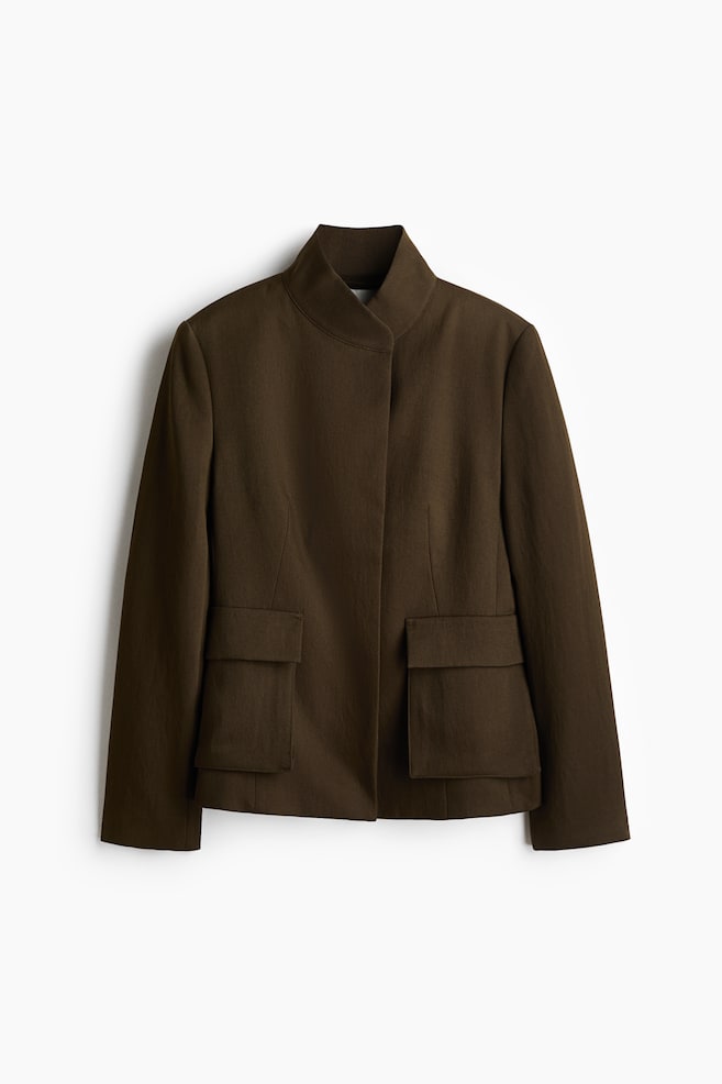 A dark brown fitted blazer is shown front on, featuring a structured stand collar and a concealed front button fastening. The jacket has defined shoulders and two large bellows pockets with flaps on the lower front. - 1