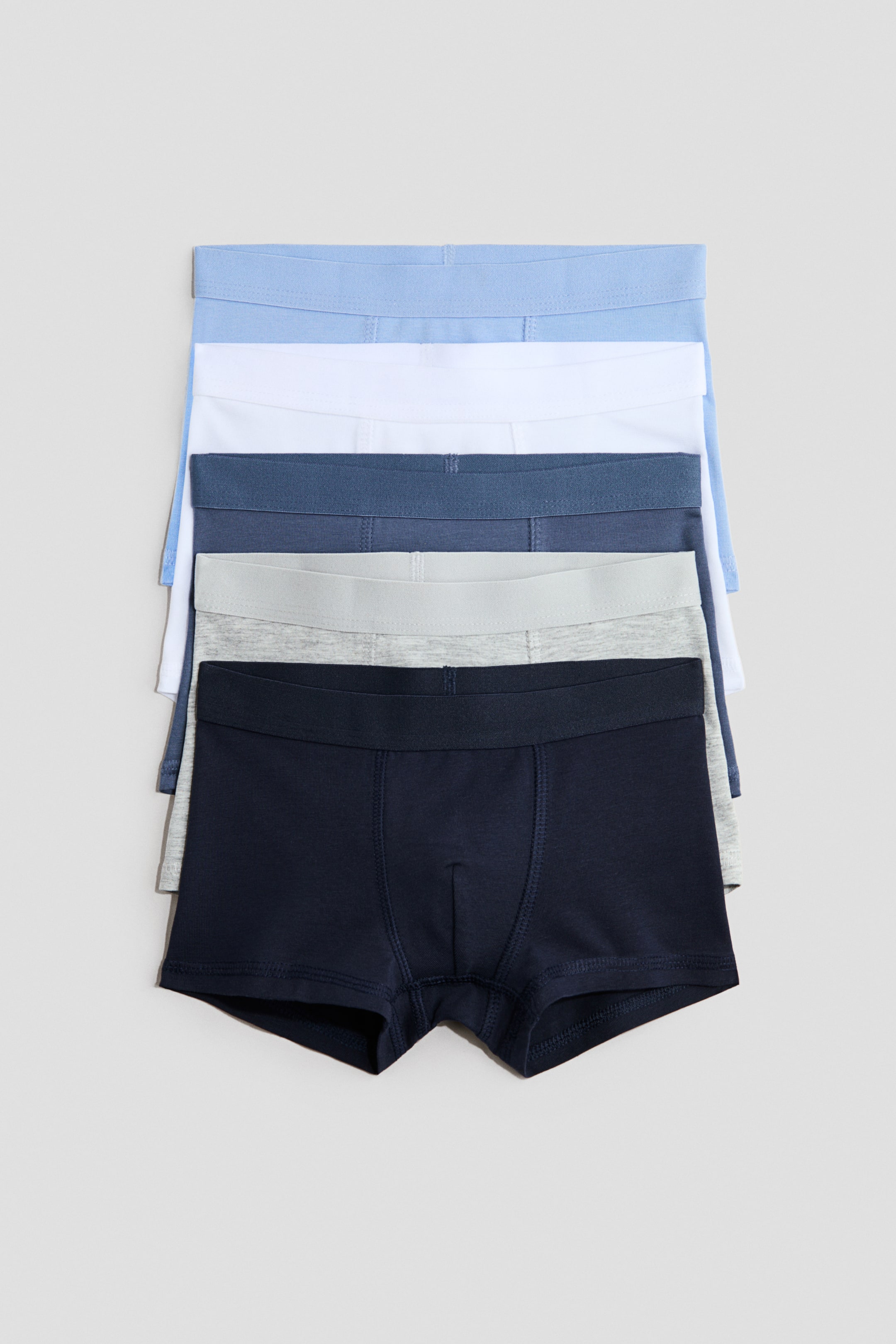 View larger image: Five pairs of trunks crafted from soft cotton jersey are neatly stacked, showcasing their front view. These trunks feature short legs, an elasticated waistband, a lined front, and come in an array of blue, white, and grey shades.