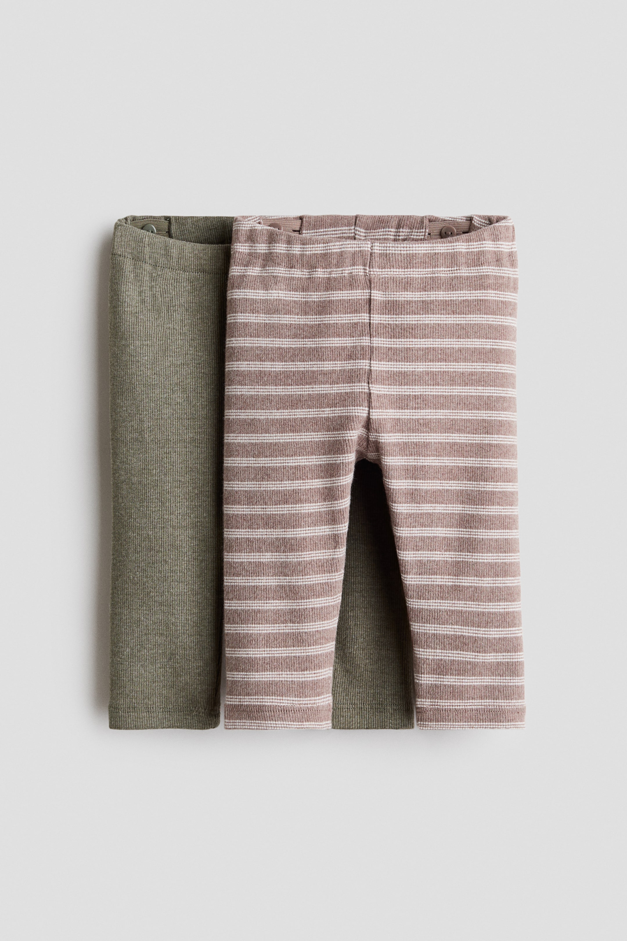 Grotere afbeelding bekijken: Twee paar H&M Adorables leggings worden plat weergegeven, met de voorkant naar voren gericht. Eén paar is effen olijfgroen, en het andere is een stoffige roos met dunne witte horizontale strepen, beide met een geribbelde jerseytextuur en een elastische tailleband met zichtbare interne knopen voor aanpassing.