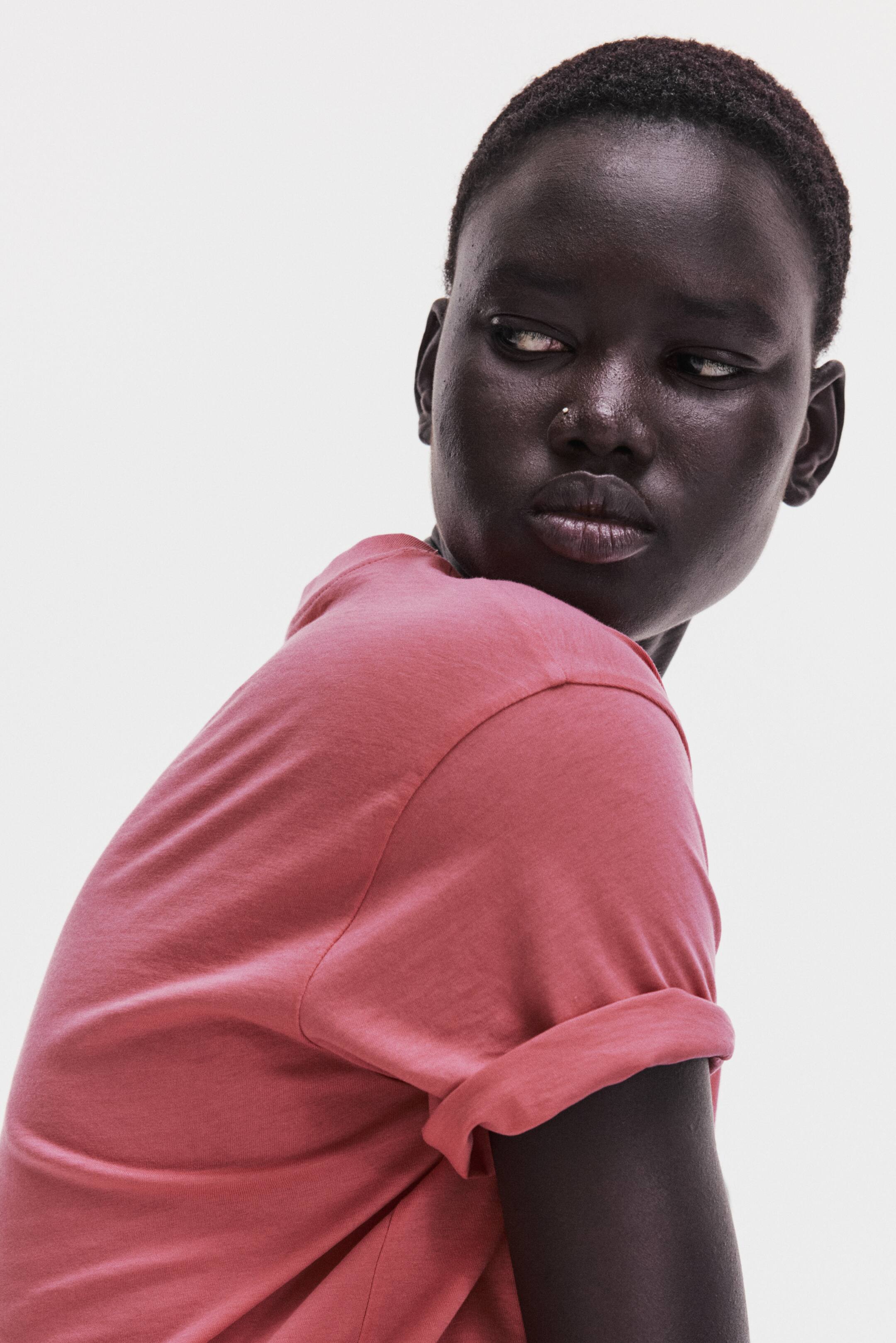 View larger image: A pink t-shirt featuring rolled-up short sleeves, a relaxed fit, and soft, jersey-like fabric, shown from a back/side angle.