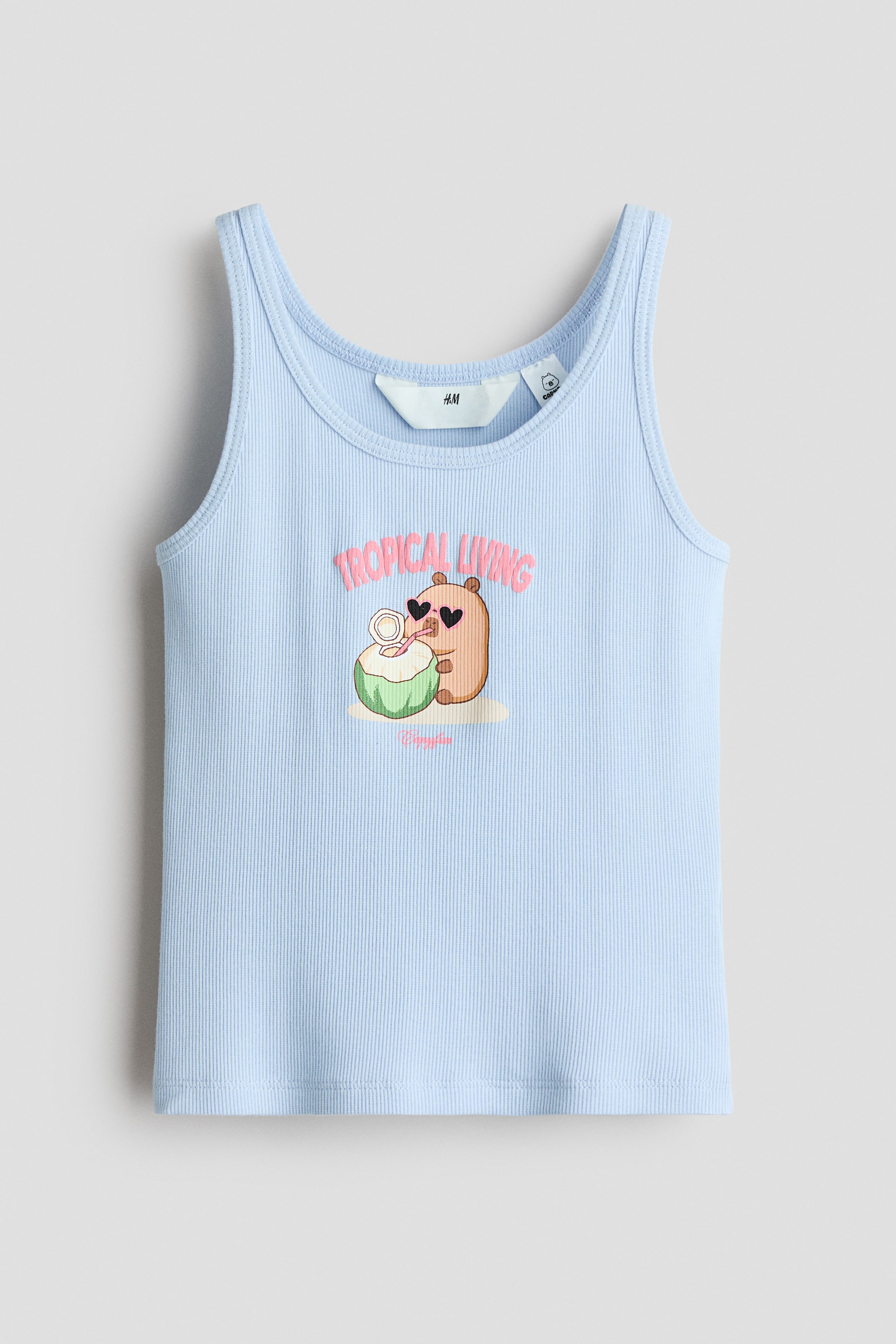 View larger image: A light blue ribbed cotton jersey vest top featuring a round neckline and narrow shoulder straps. The front displays a print motif of a brown cartoon animal wearing heart-shaped sunglasses and sipping from a green coconut, with pink text above reading 'TROPICAL LIVING'.