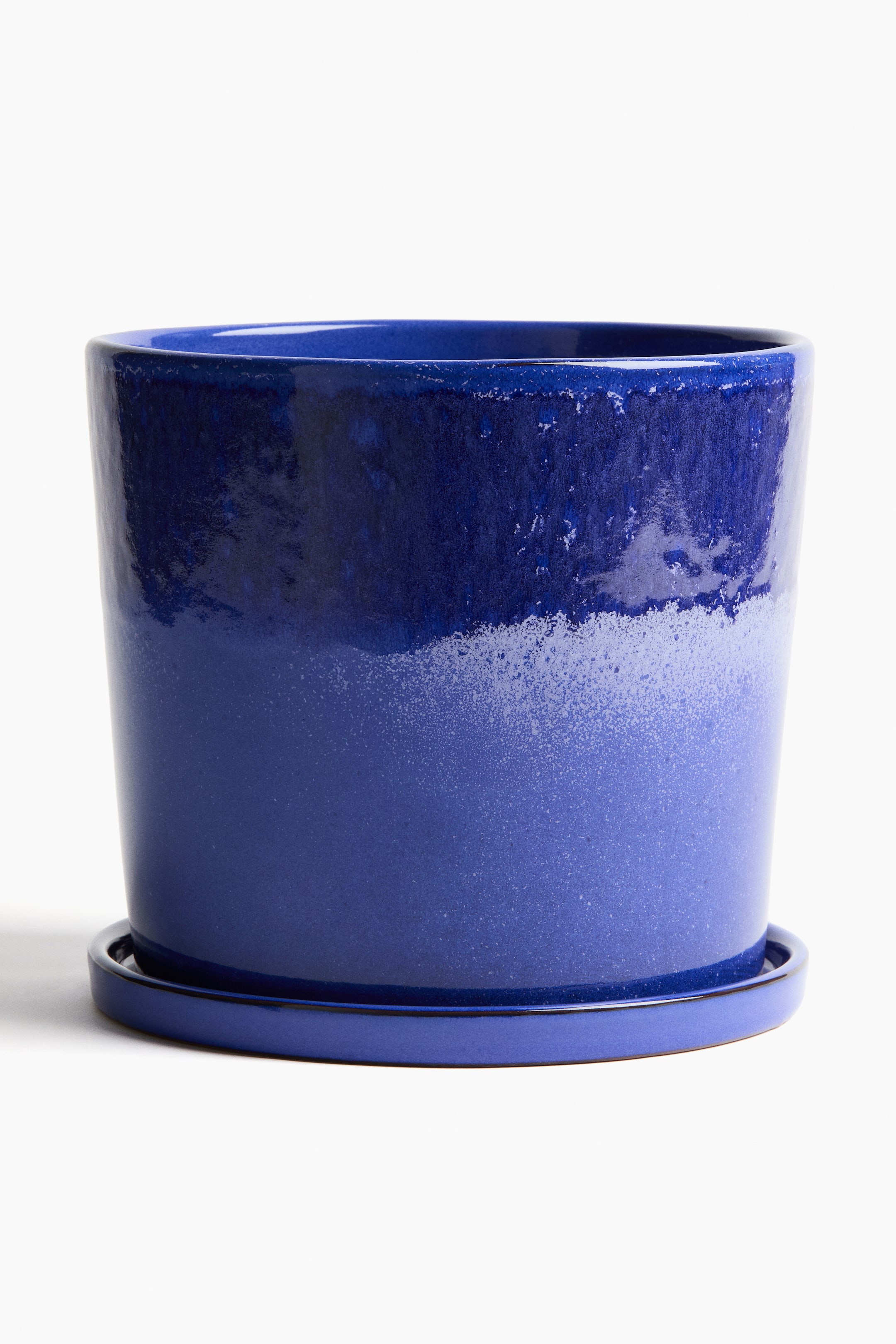 Visualizza immagine più grande: Un grande vaso per piante in terracotta smaltata presenta una finitura a gradiente blu, che passa da una sezione superiore scura e lucida a una sezione inferiore più chiara e punteggiata, ed è dotato di un foro di drenaggio sul fondo. È posizionato su un sottovaso abbinato di colore blu, con il vaso che misura 23 cm in altezza e 21 cm di diametro superiore, mentre il sottovaso ha un diametro di 23,1 cm.