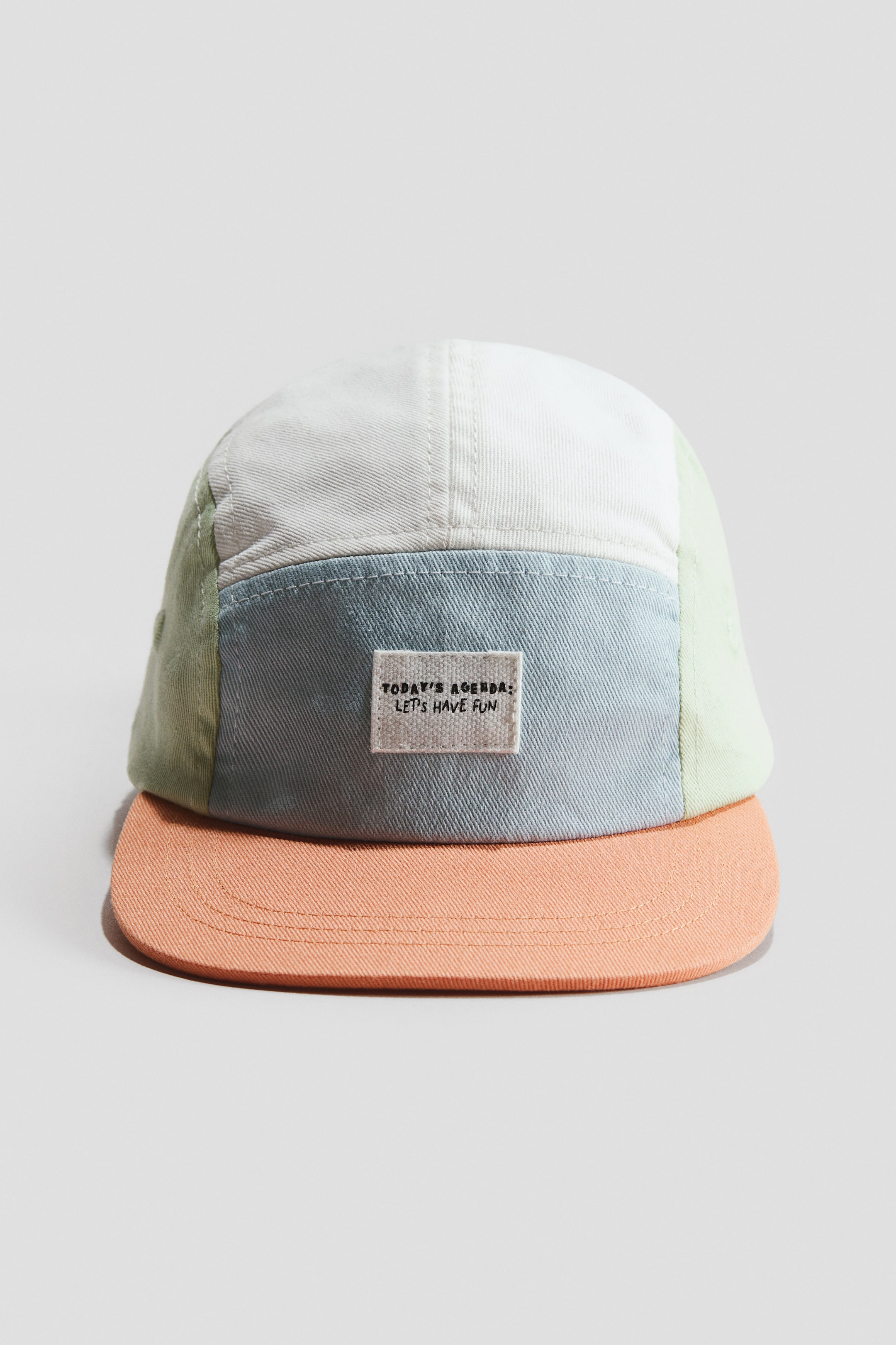 Agrandir l'image: La casquette en coton présente sa vue de face, avec un design en blocs de couleurs composé de panneaux crème clair, bleu clair et vert clair formant la couronne, et une visière plate corail s'étendant à l'avant. Un petit patch rectangulaire affichant "TODAY'S AGENDA: LET'S HAVE FUN" est cousu sur le panneau avant bleu clair.