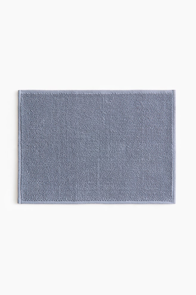 This rectangular blue-grey bath mat showcases its textured surface, adorned with small, dense loops. The mat is completed with a flat, woven border along its edges. - 1