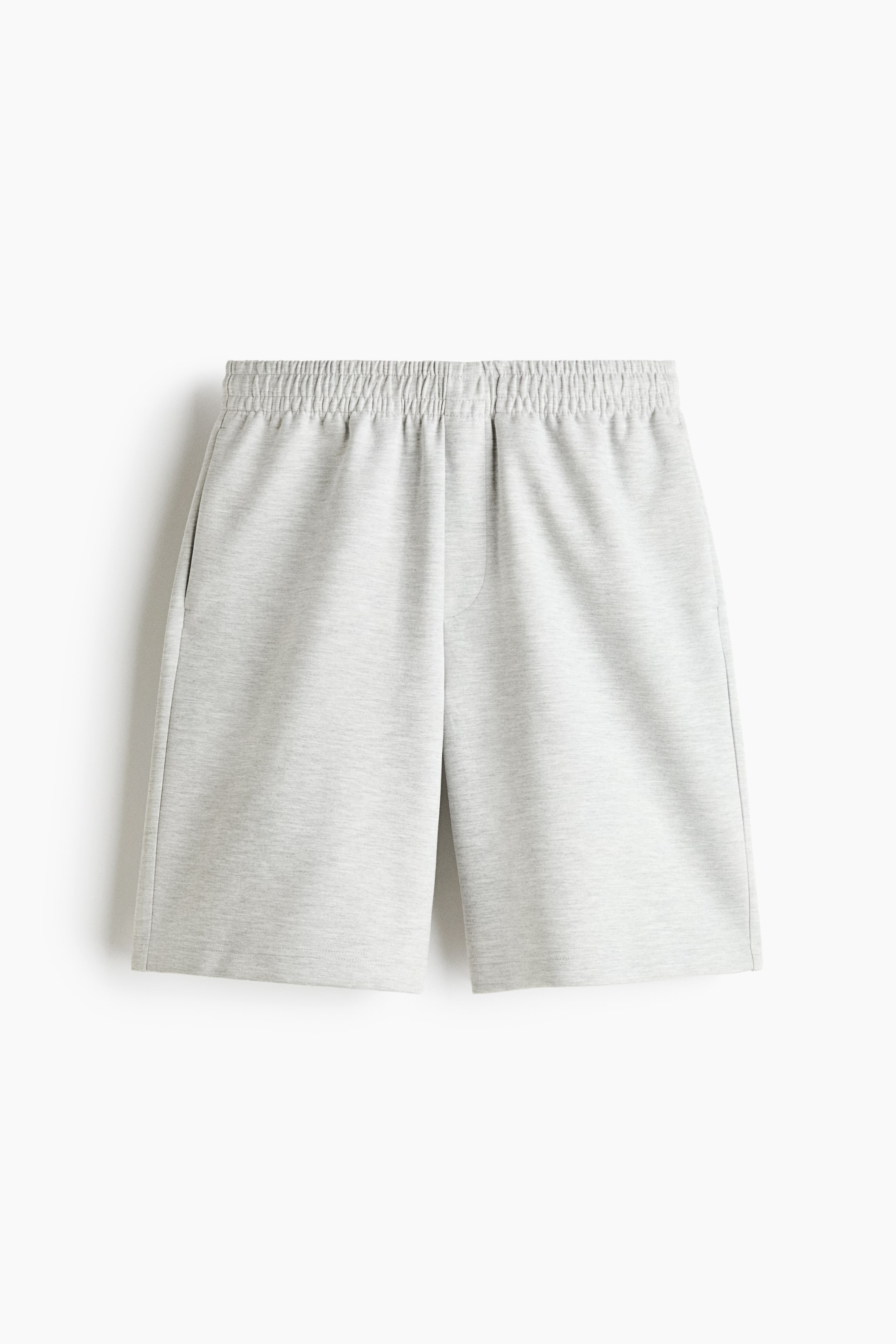 View larger image: Light grey knee-length sweat shorts are shown from the front, featuring a relaxed fit, a smocked elastic waistband, and a mock fly. The design is crafted from a smooth interlock fabric and includes subtle side pockets.