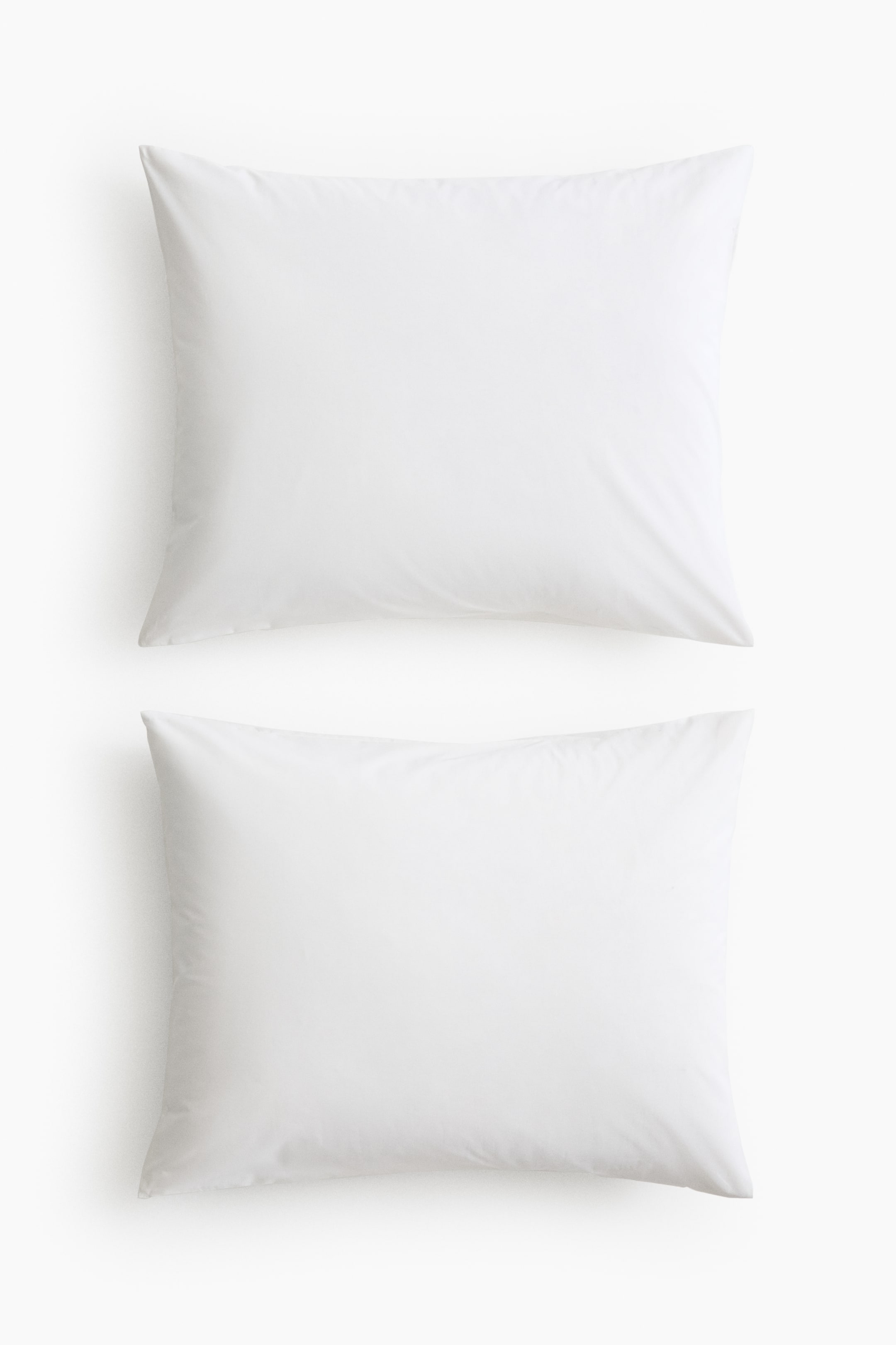 View larger image: A pair of white rectangular pillowcases in a soft cotton weave are laid flat, one positioned above the other. Their smooth fabric surface displays subtle creases.