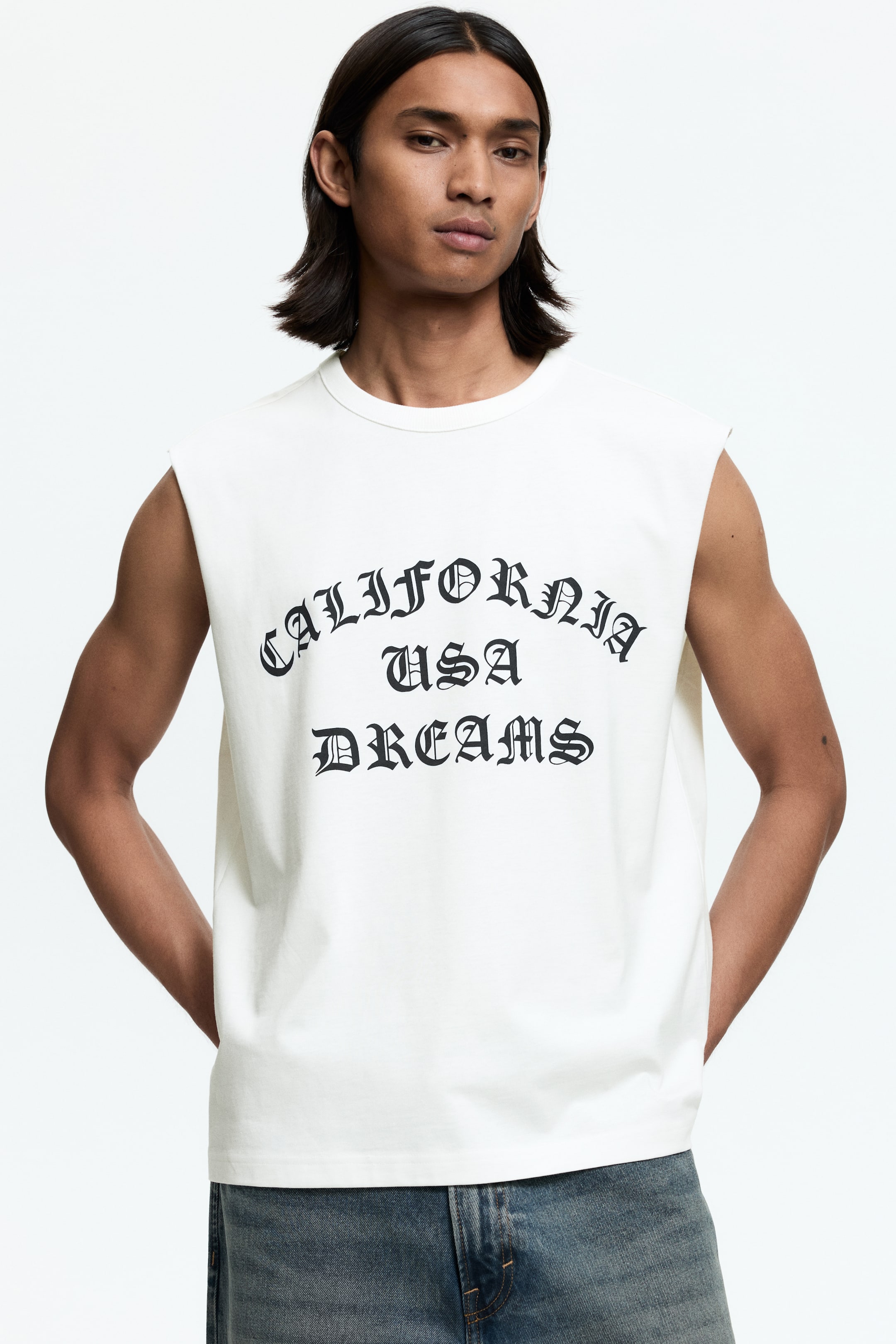 Ver imagen más grande: La modelo lleva puesto un top de tirantes de jersey de algodón color crema. Presenta un escote redondo con ribete y un estampado en negro "CALIFORNIA USA DREAMS" en la parte delantera, con un dobladillo recto y un corte holgado.