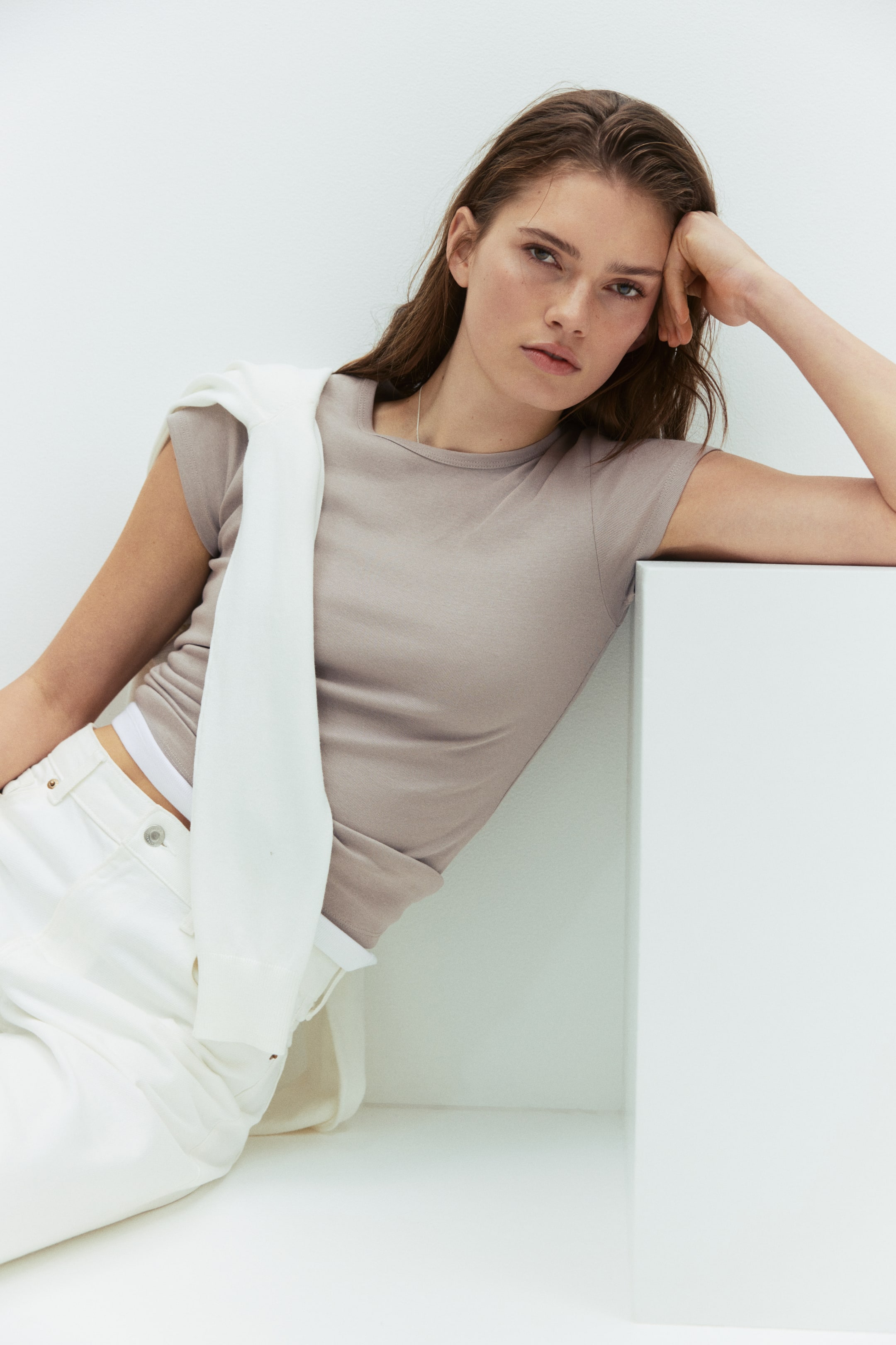查看大圖: 淺灰褐色T恤為圓領短袖，剪裁貼合身形。白色毛衣搭於左肩，部分覆蓋T恤；白色抹胸從T恤下擺微微露出。