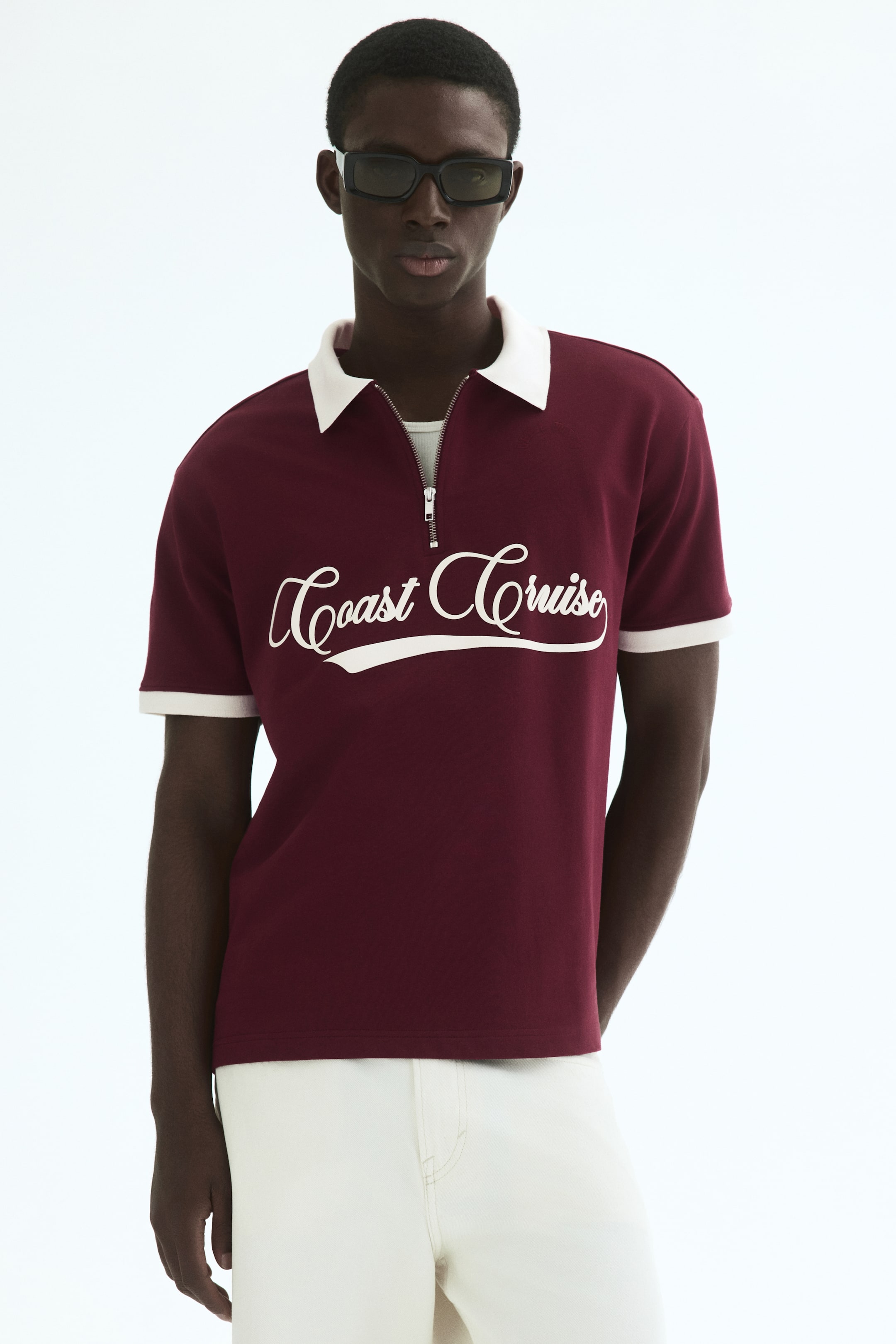 View larger image: Presenting a burgundy polo shirt, showcasing a white collar, a half-zip closure that reveals a white undershirt, and short sleeves adorned with white banding. The phrase "Coast Cruise" is elegantly emblazoned in white script across the chest.