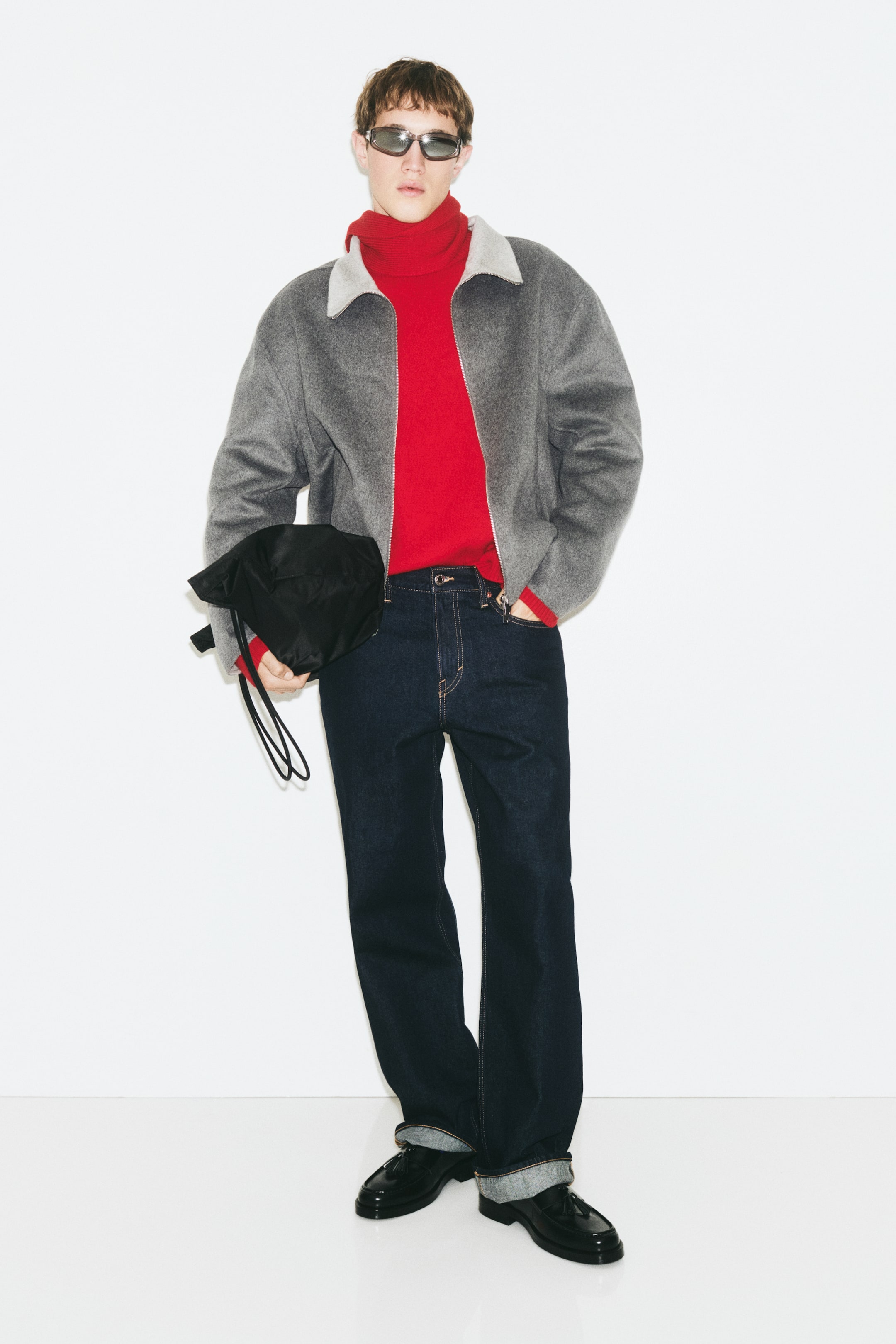 Ampliar la imagen: Una sobrecamisa de mezcla de lana en color gris, con acabado cepillado y cuello gris claro en contraste, la lleva la modelo abierta. La sobrecamisa presenta hombros caídos y se combina con un suéter de cuello alto en rojo brillante y jeans azul oscuro.