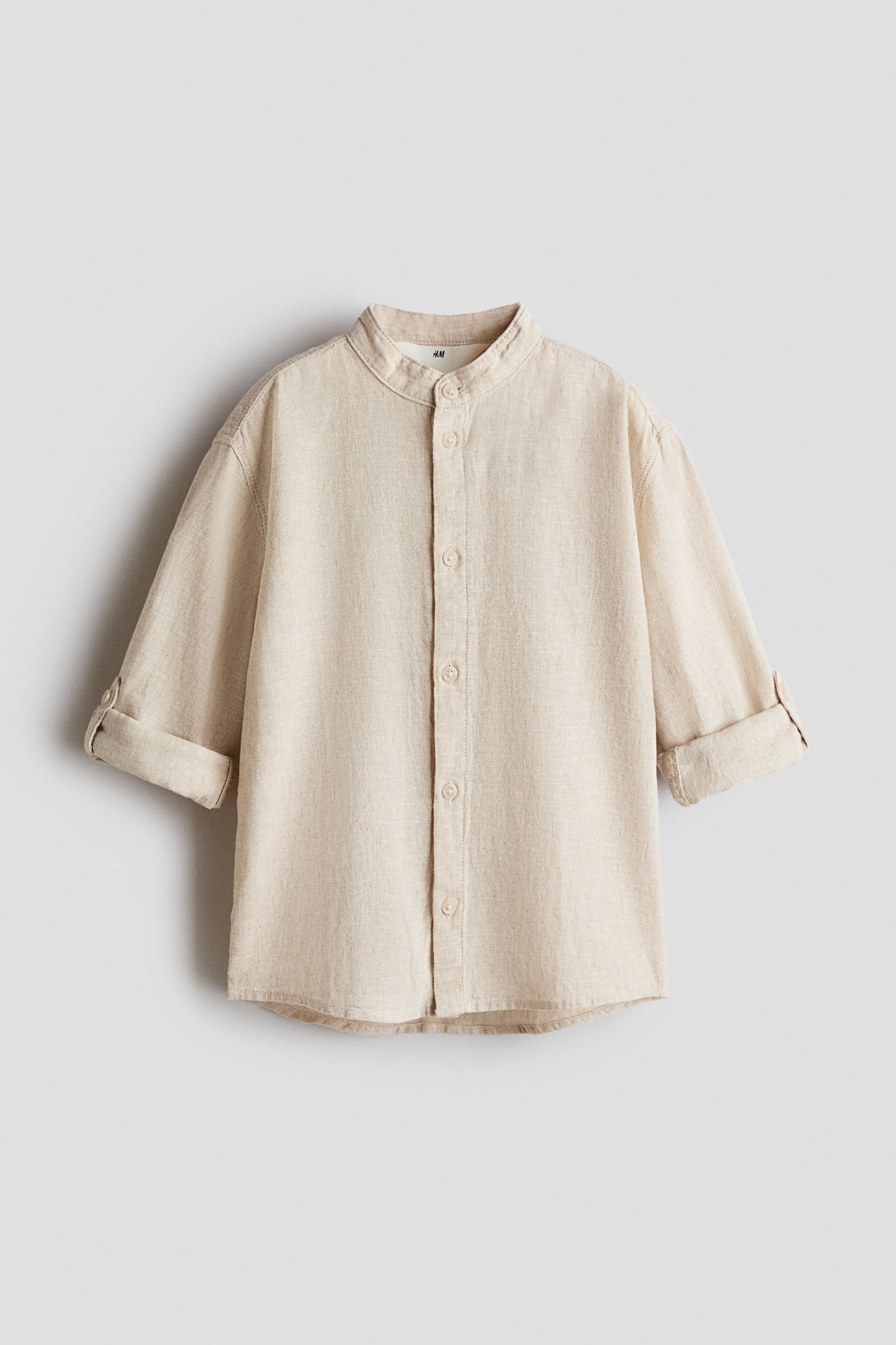 View larger image: A beige woven shirt is shown from the front, featuring a band collar and a button-up front. The long sleeves have rolled-up cuffs secured with a button and tab.