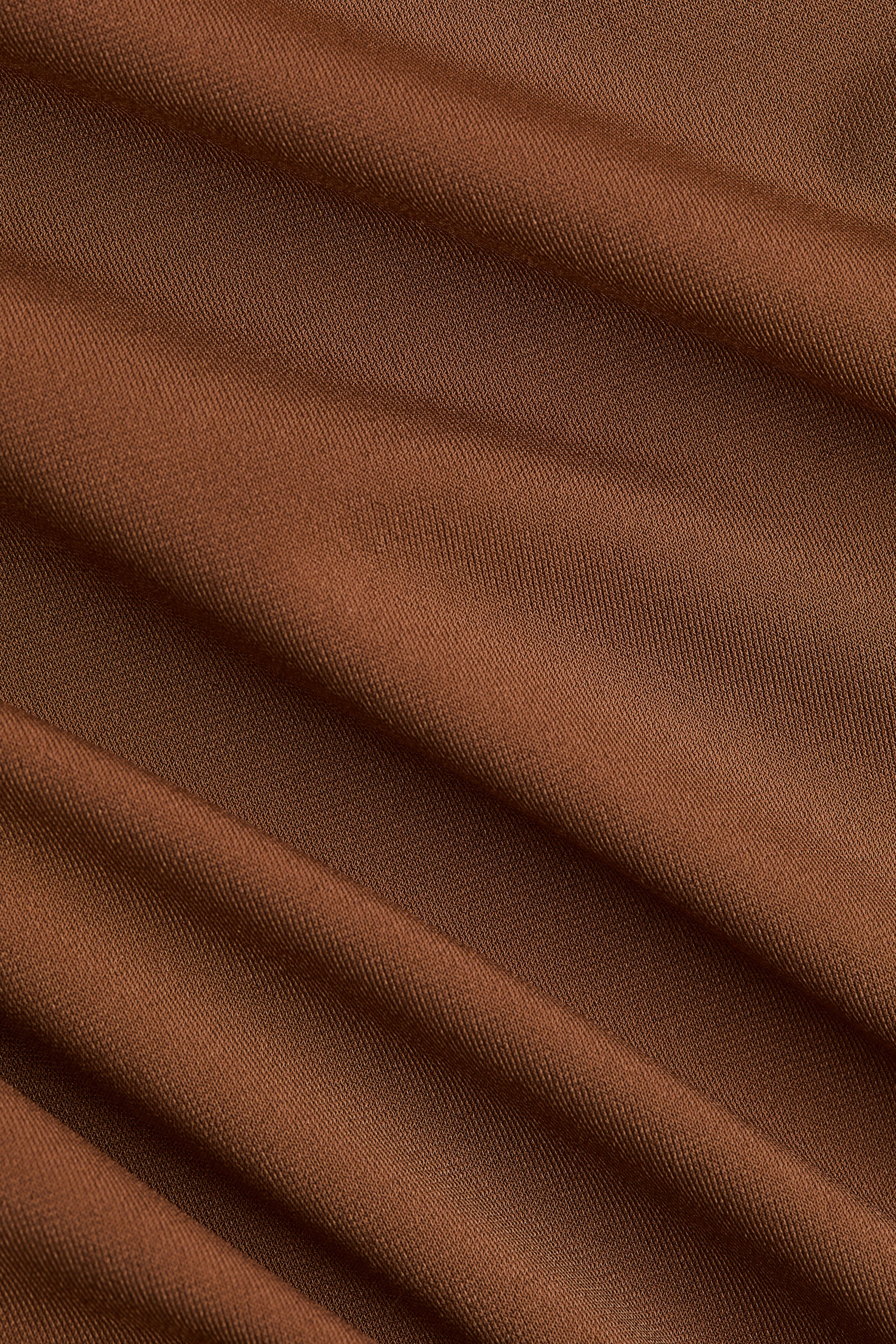Vis større bilde: Et brunt stoff viser et distinkt diagonalt vevemønster og henger i myke, bølgende folder.
