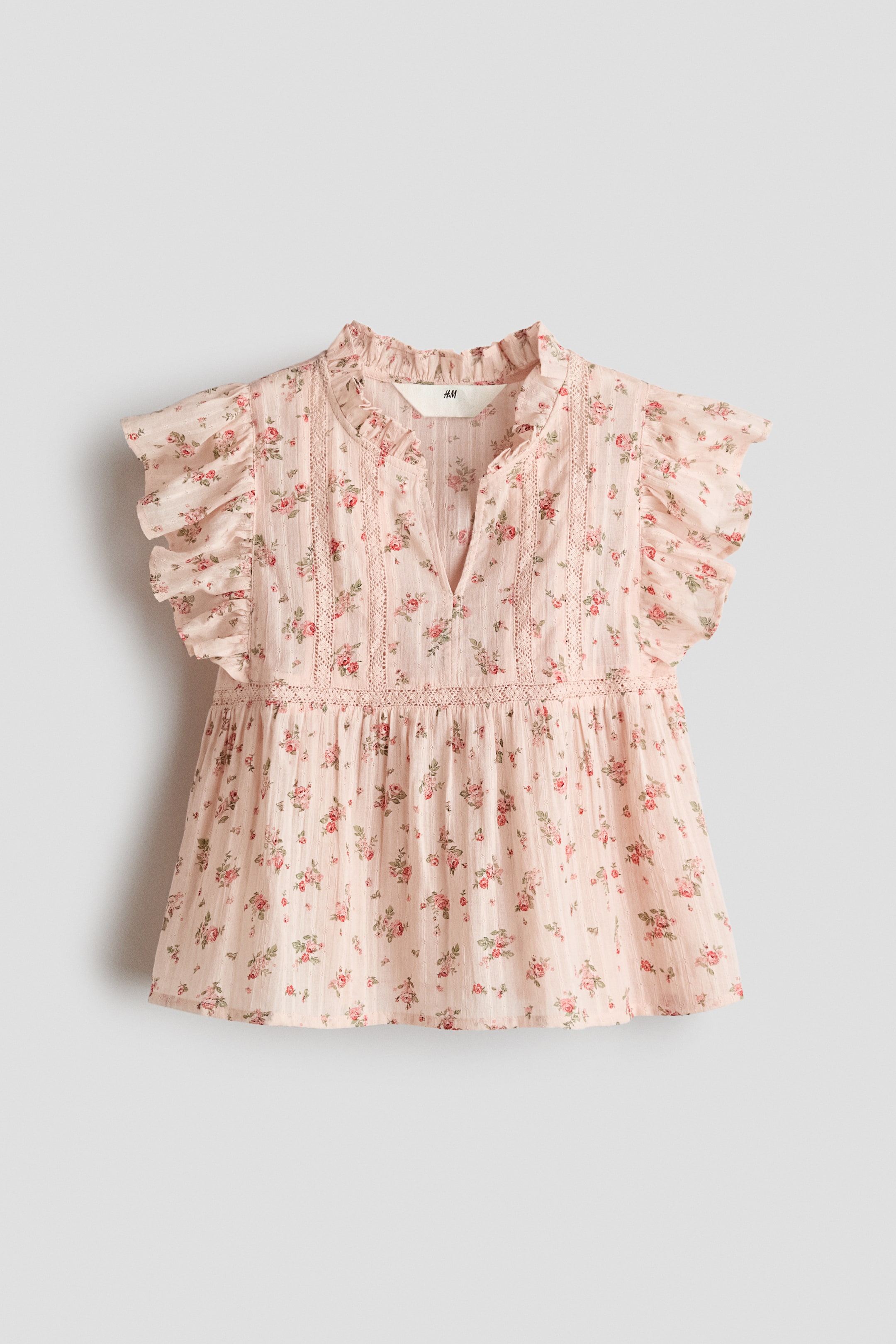 Visualizza immagine più grande: Una blusa svasata, realizzata in un tessuto di cotone leggero, presenta un motivo floreale di rose rosa e rosse, un colletto arricciato con un'apertura a V sul davanti, maniche svolazzanti e inserti in pizzo sul corpetto e in vita.