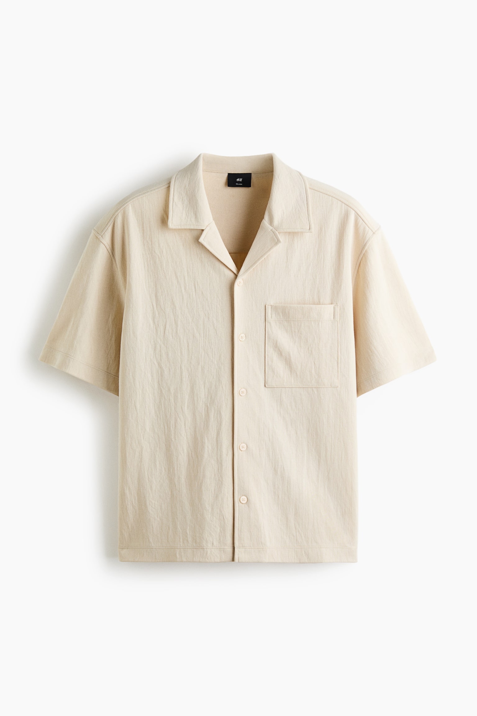 Má»t chiếc áo jersey interlock mà u be tay ngắn ÄÆ°á»£c chụp từ phÃa trưá»c, có phom dáng thoải mái và cá» resort. Ão có kiá»u French front vá»i các nút cùng mà u, má»t túi Äắp á» ngá»±c trái và lai áo cắt thẳng.