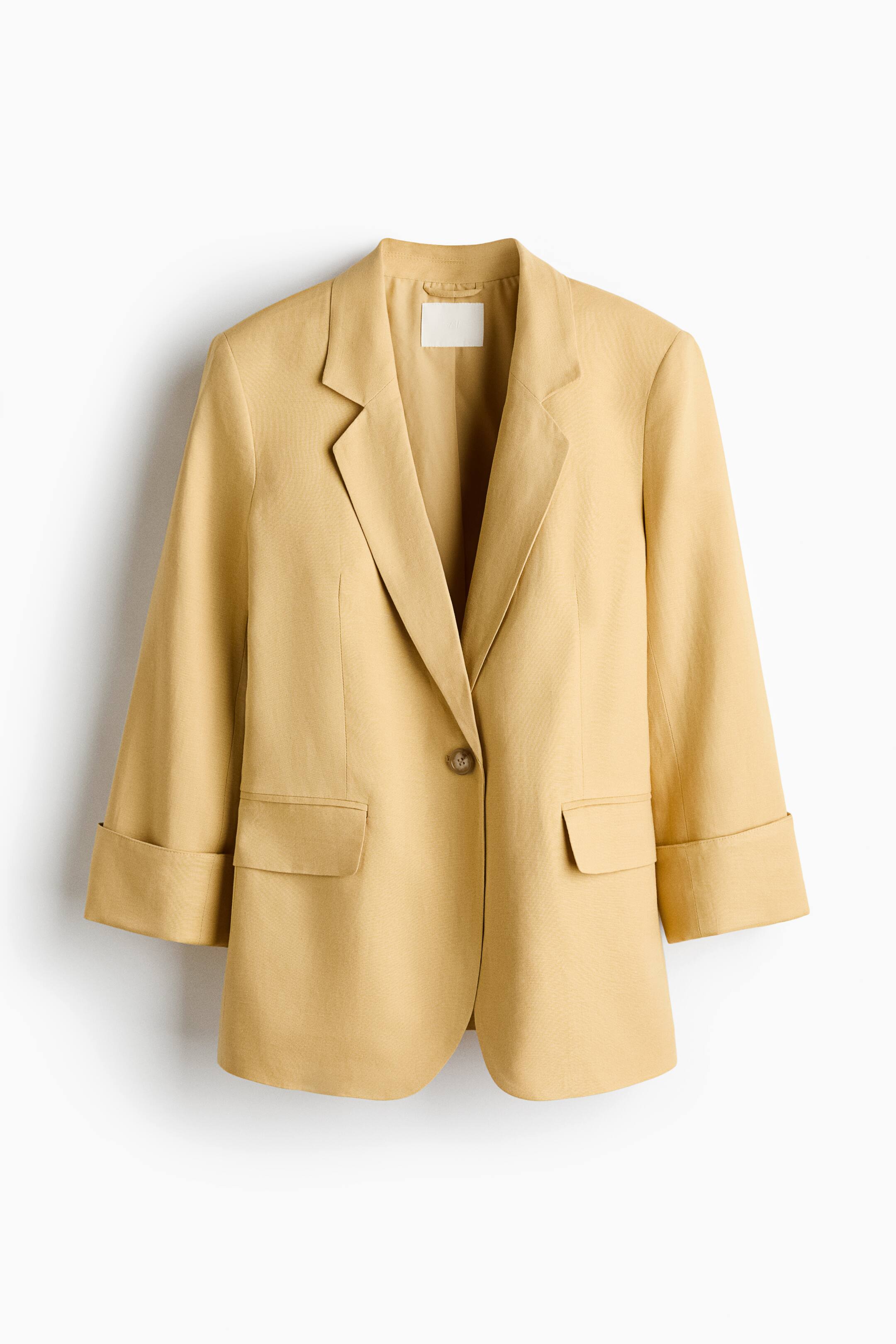 View larger image: The tan blazer is showcased in a front view, highlighting its notch lapels and single-button closure. Two flap pockets can be seen on the front, with the sleeves stylishly rolled up into wide cuffs.