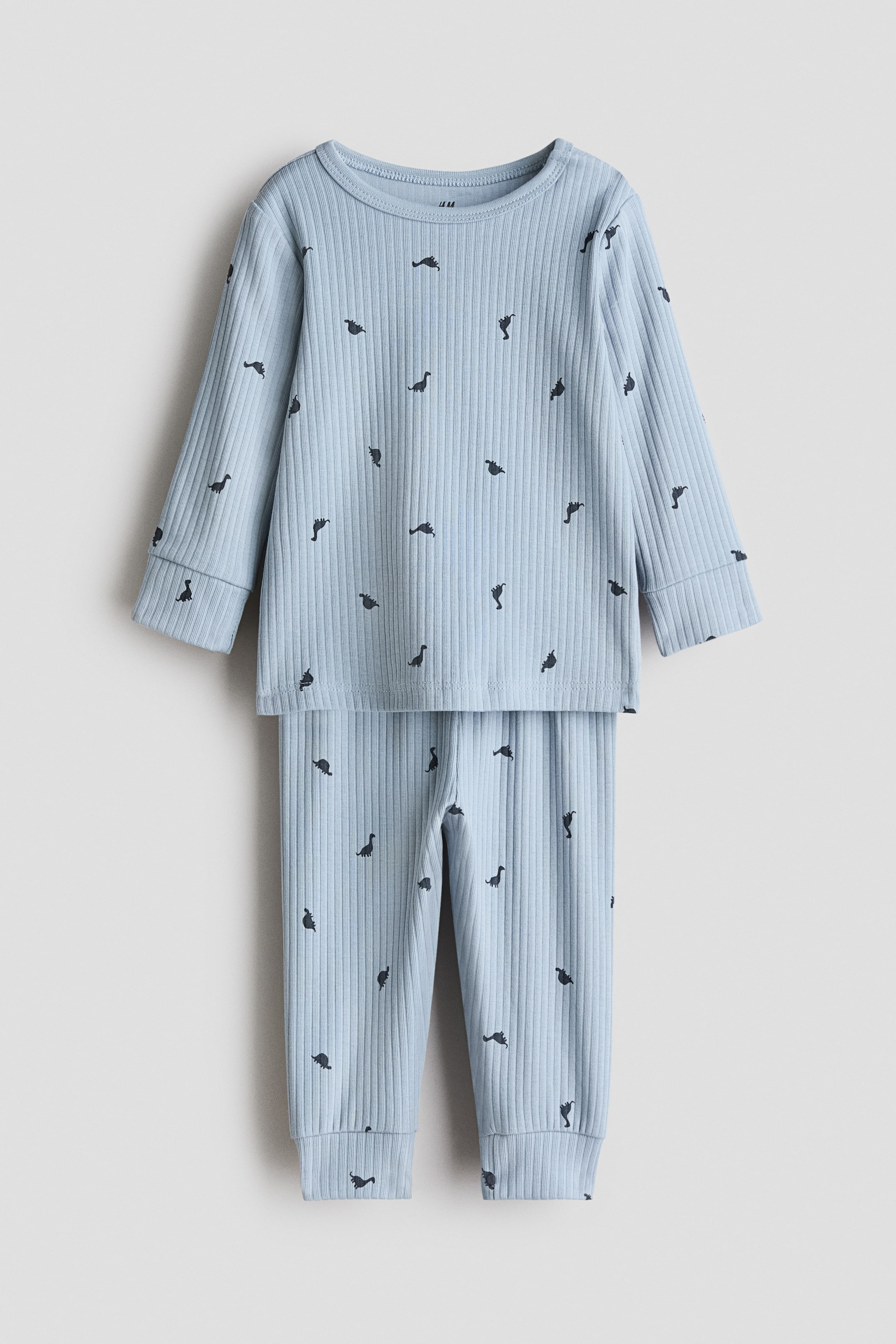 View larger image: A light blue ribbed cotton set shown from the front, featuring a long-sleeved top with a crew neck and ribbed cuffs, and matching long pants with ribbed ankle cuffs; both pieces are patterned with small dark dinosaur silhouettes.