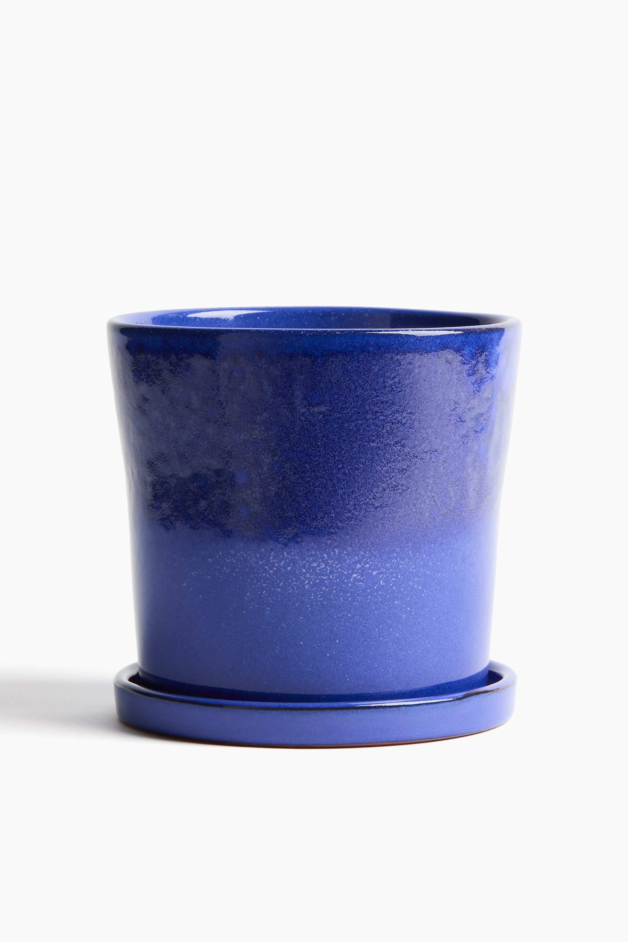 Grotere afbeelding bekijken: Een geglazuurde terracotta plantenpot en bijpassende schotel zijn naar voren gericht. De pot heeft een ombre blauwe glazuur, die overgaat van een donkerblauw aan de bovenkant naar een lichter blauw aan de onderkant, en rust op de ronde schotel.