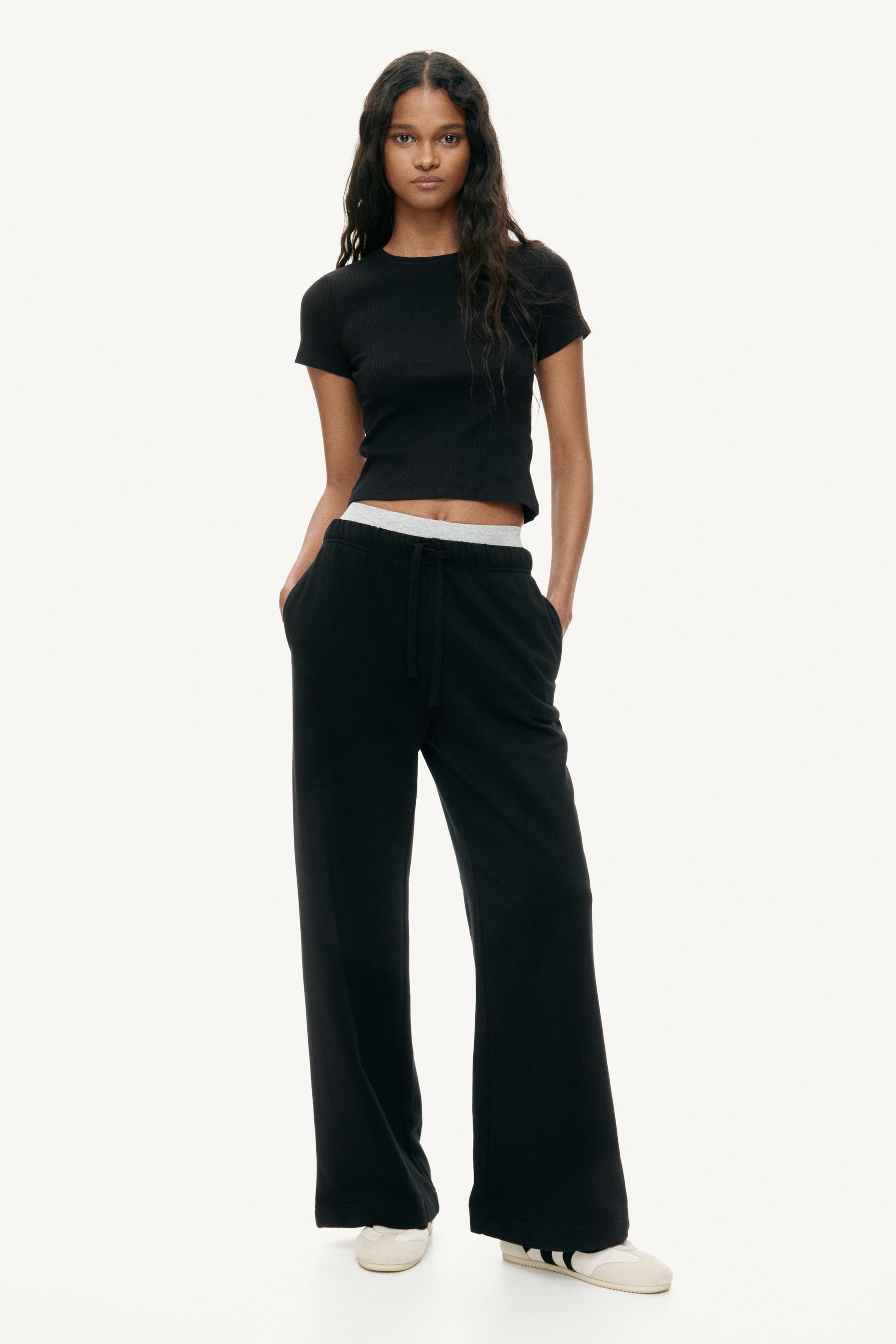 View larger image: A black ribbed cropped t-shirt with short sleeves and a crew neck is paired with black wide-leg sweatpants, showcasing a grey waistband and a drawstring fastening.