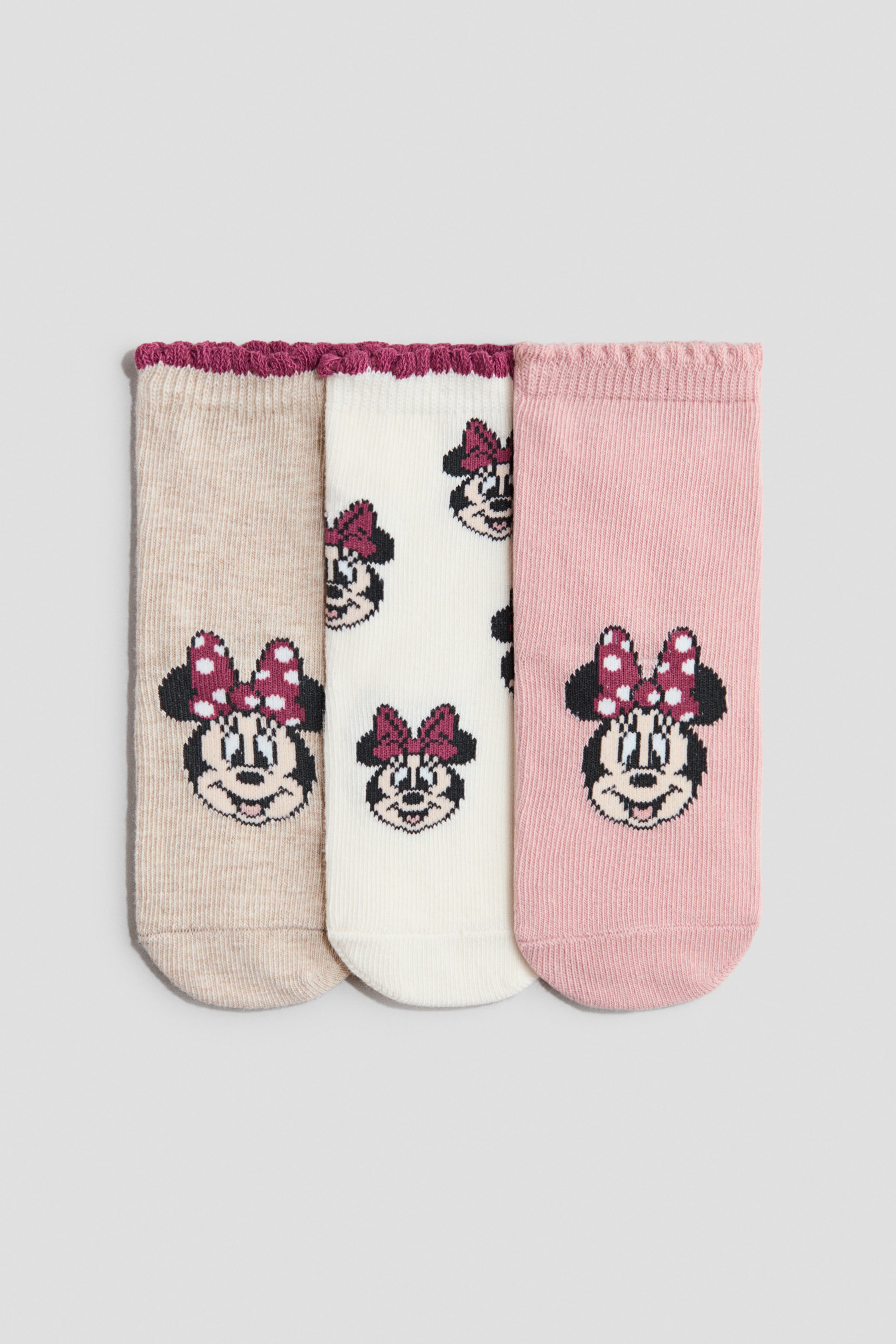 View larger image: Three ankle socks are laid flat, showcasing their front. The beige and pink socks each highlight a large Minnie Mouse face adorned with a polka-dot bow near the toe, while the off-white sock features multiple smaller Minnie Mouse faces with polka-dot bows in an all-over pattern. All socks display ruffled cuffs, with the beige and off-white socks having maroon cuffs, and the pink sock featuring a matching pink cuff.